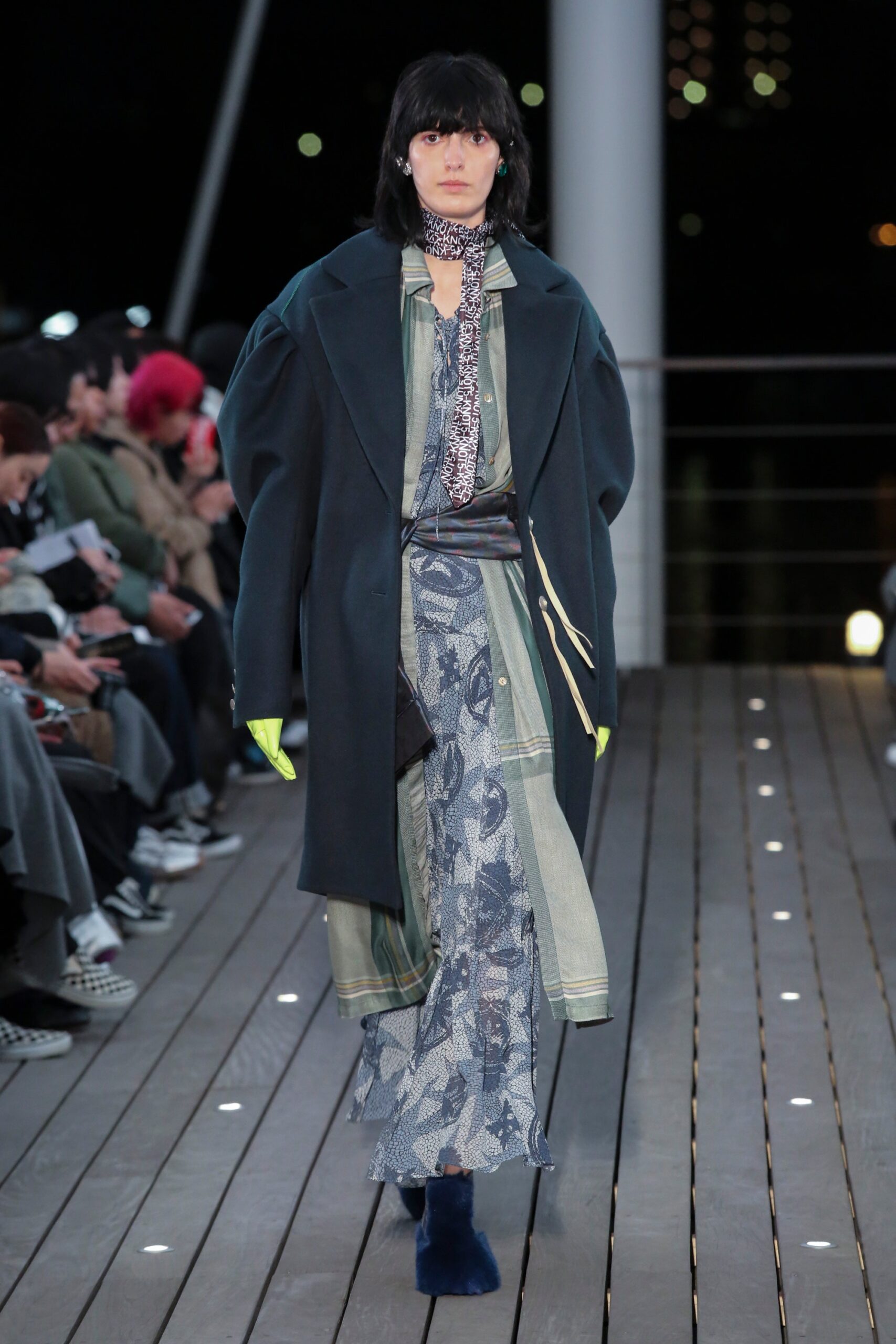 A relaxed green coat layered over a blue dress with long sleeves and a collared neckline.