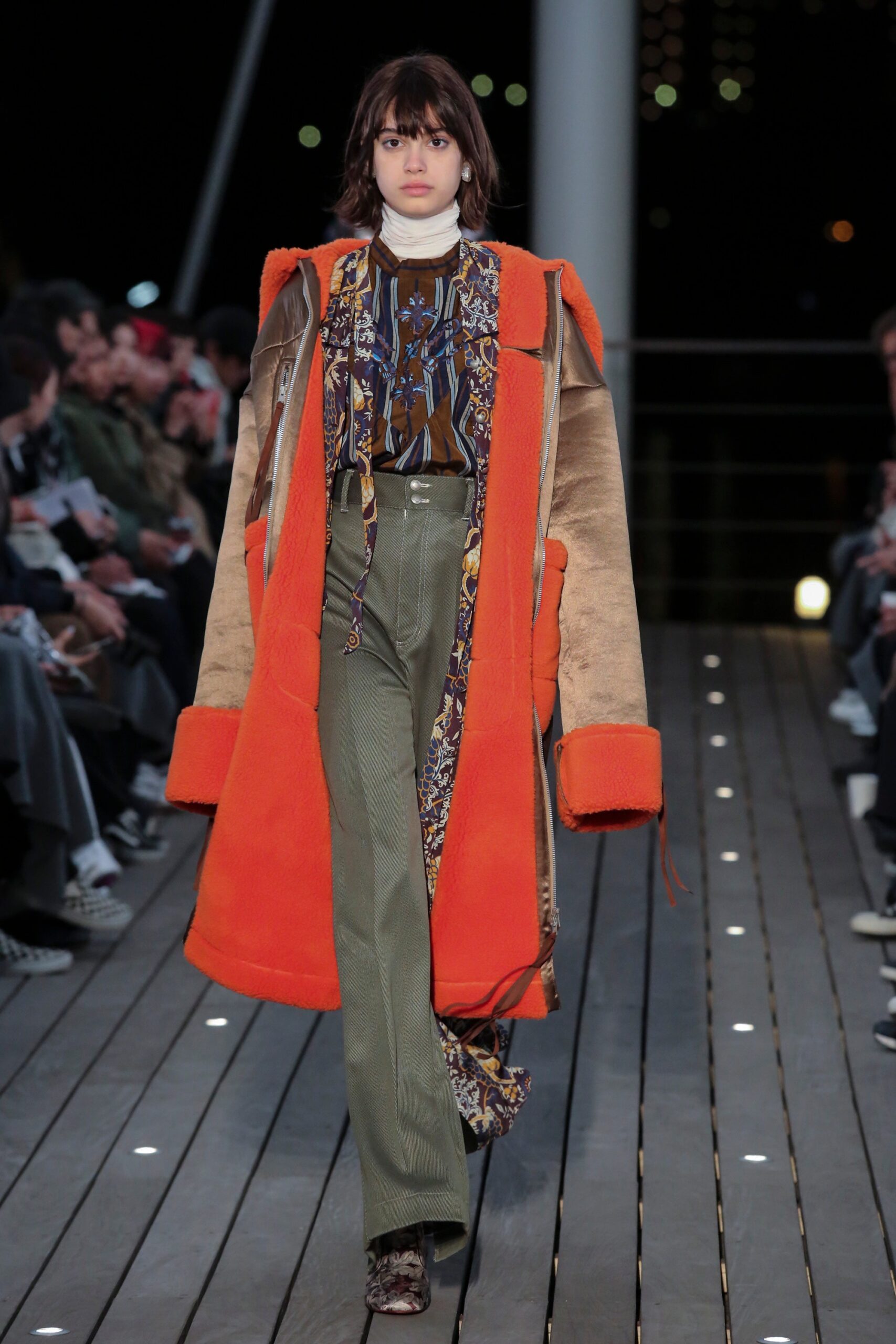 A relaxed orange coat paired with flared green pants, featuring a long-sleeve and collared design.