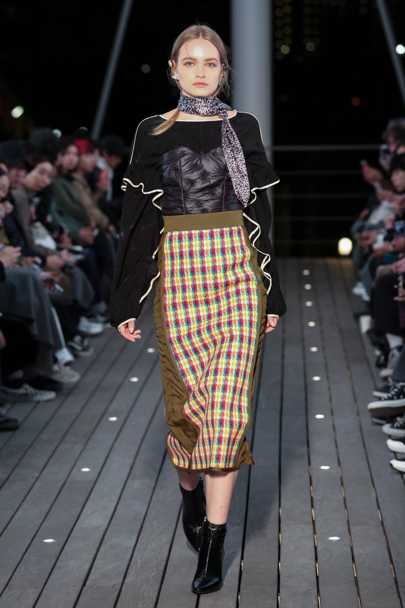 A fitted black long-sleeve top with ruffled details paired with a multicolor checked skirt.