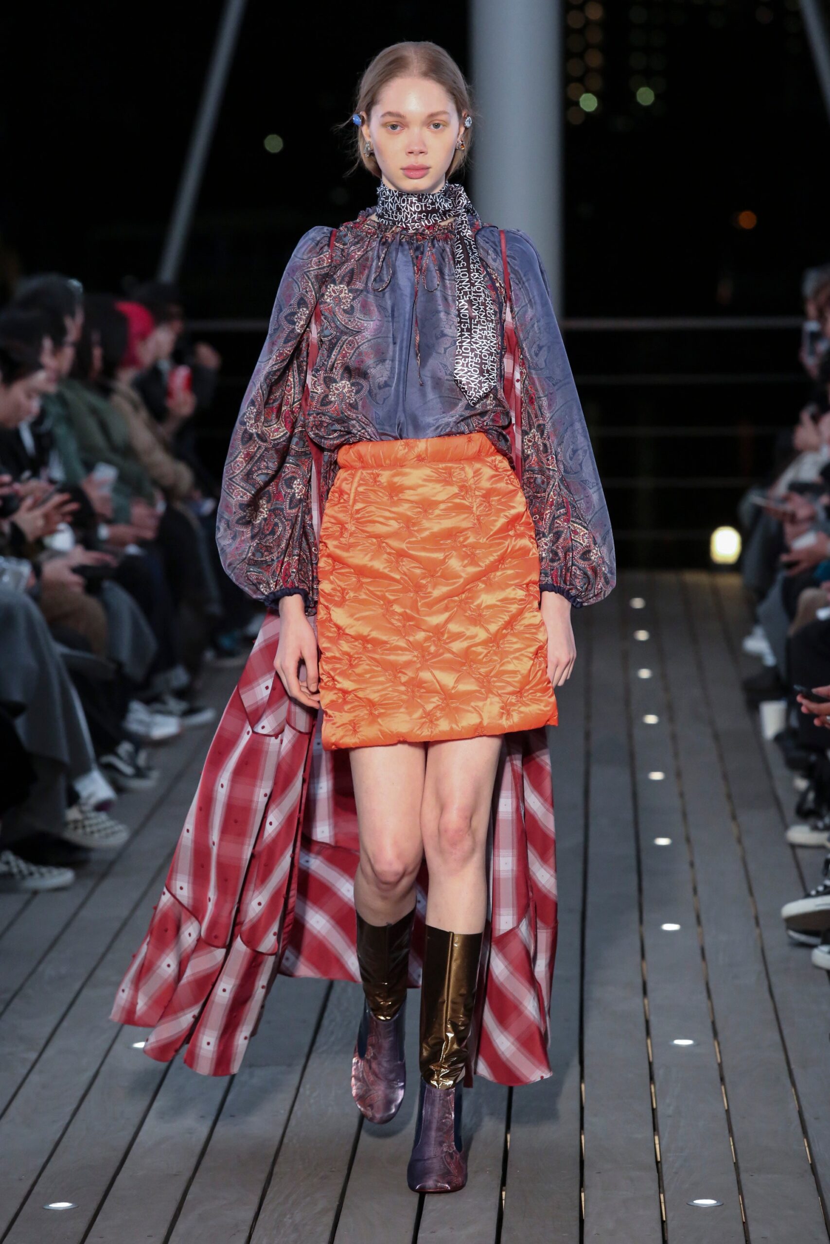 A fitted blue silk long-sleeve blouse paired with a pleated orange skirt featuring an asymmetric design.
