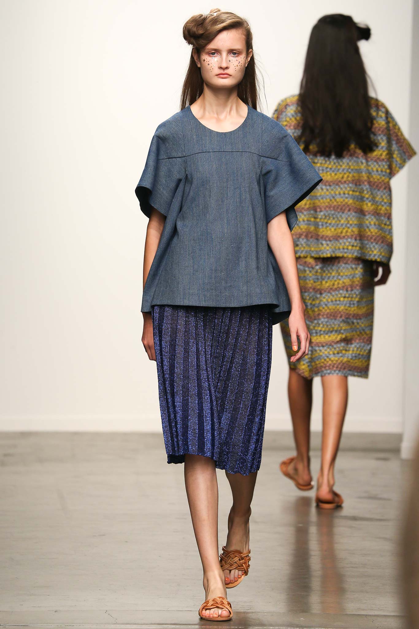 A relaxed blue denim top with short sleeves paired with a pleated skirt.