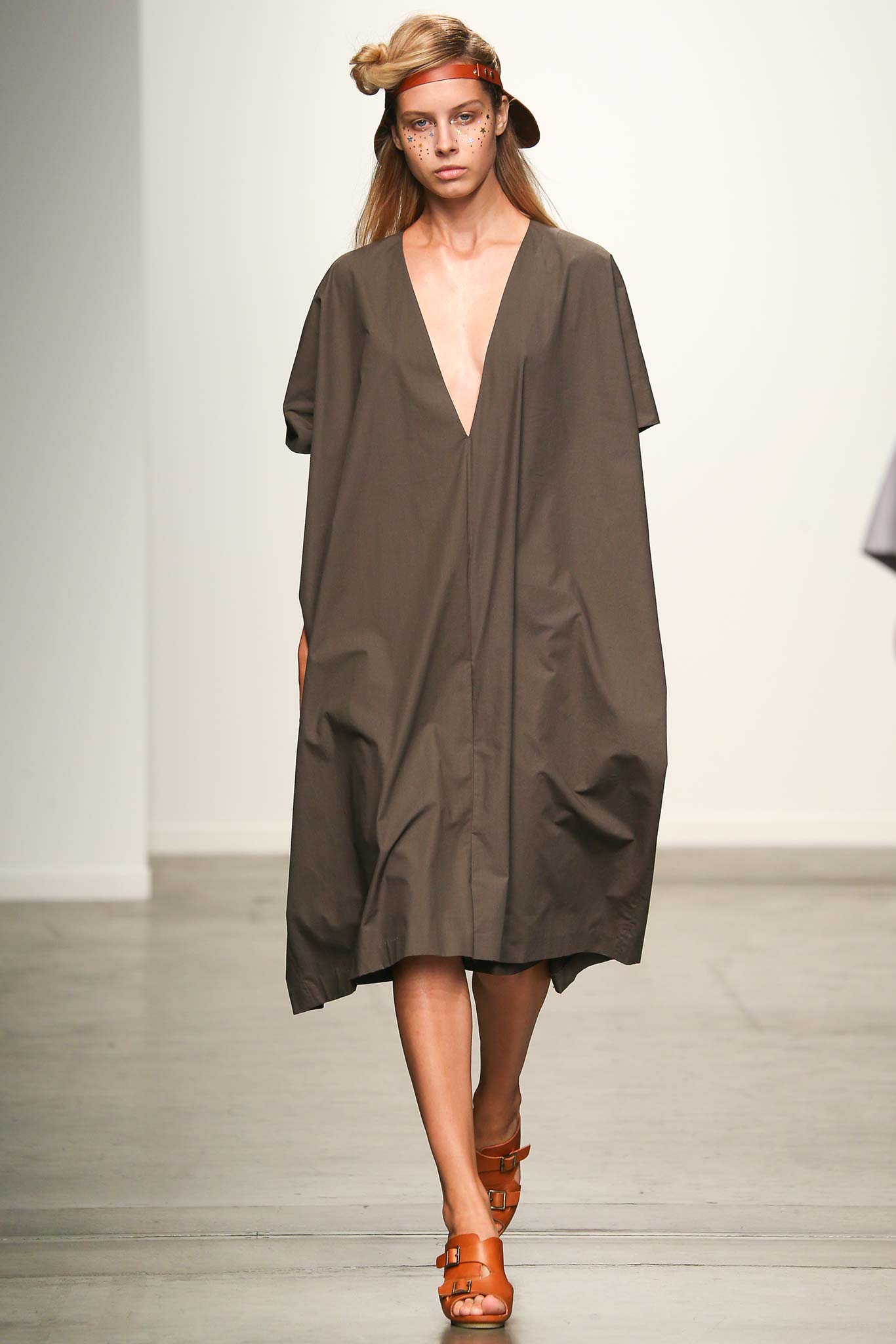 A relaxed brown cotton sleeveless dress with a deep V-neckline and asymmetric design.