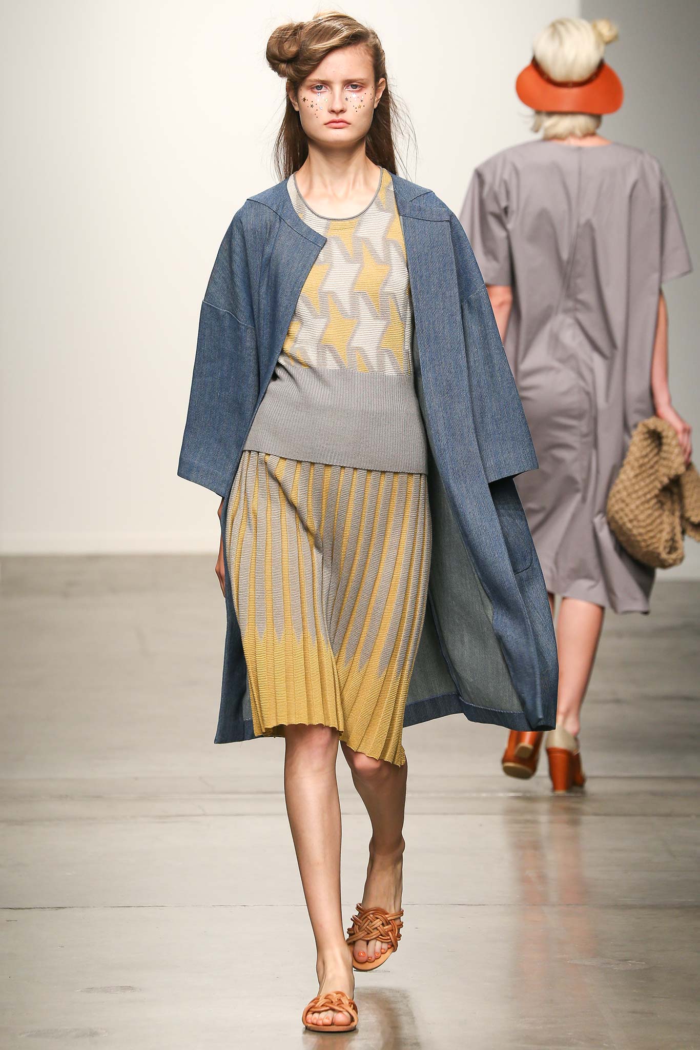 A relaxed gray dress with pleated details, layered under a denim coat.