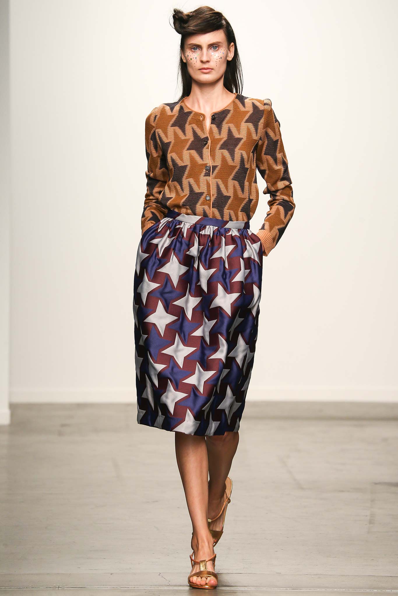 A relaxed brown printed blouse with long sleeves paired with a pleated blue skirt.