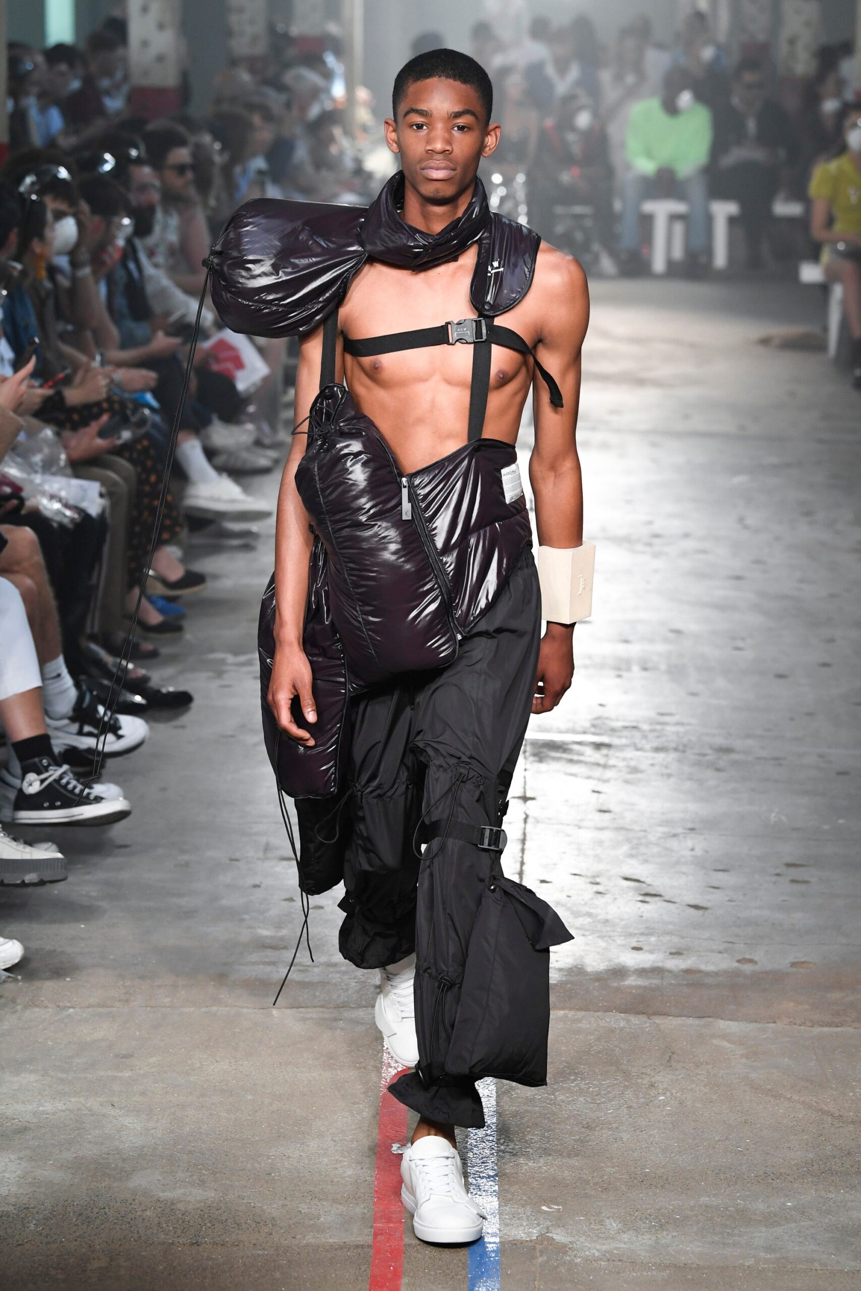 This ensemble features a relaxed, sleeveless jacket crafted from black nylon, distinguished by its asymmetric design and unique collar. The accompanying pants complement the jacket's avant-garde aesthetic, showcasing a blend of functionality and contemporary style through their zippered details.