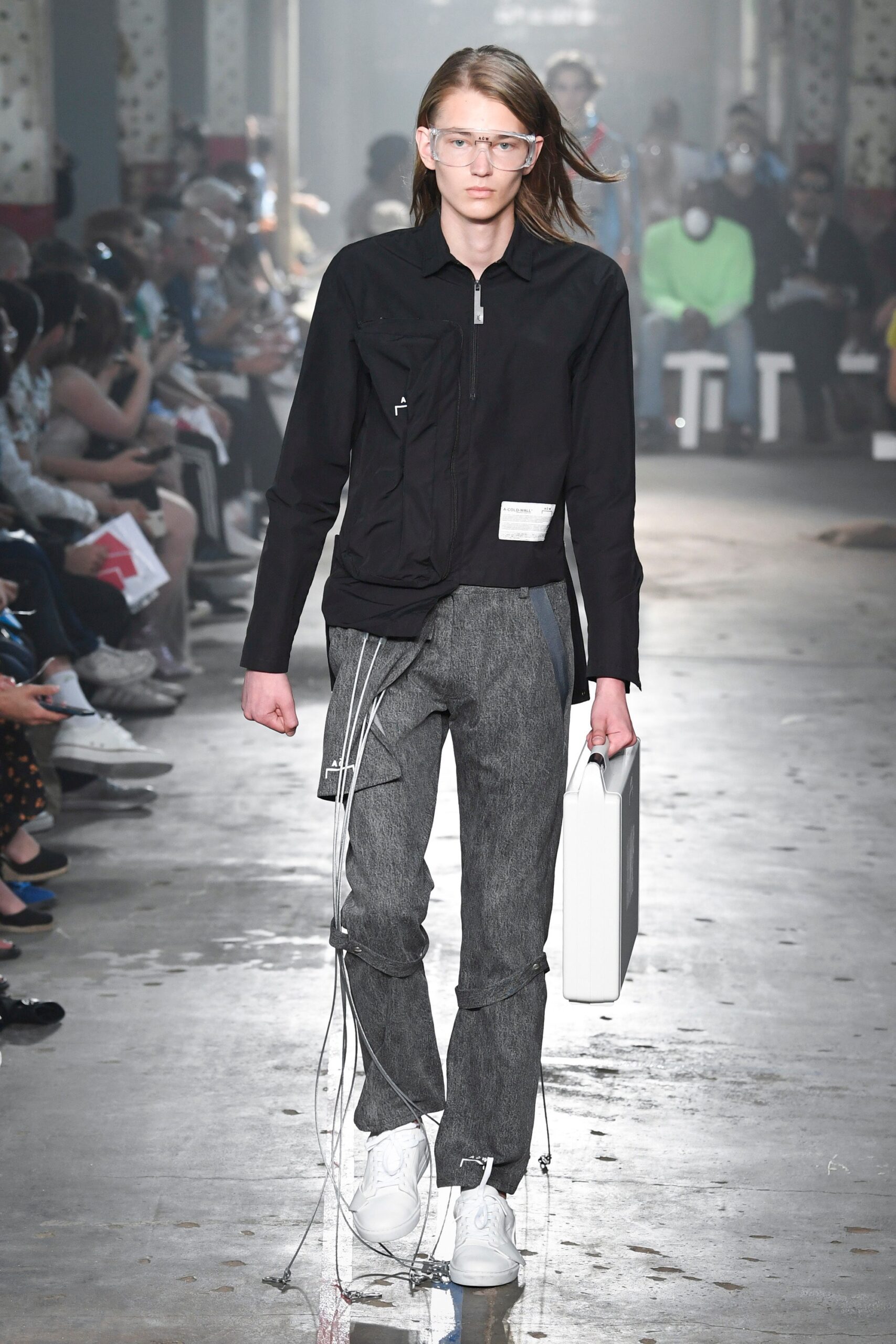 This ensemble features a relaxed black jacket with a distinctive zippered detail, complemented by straight-leg gray pants. The combination creates a modern silhouette that balances structure with casual ease, making it a versatile choice for contemporary styling.