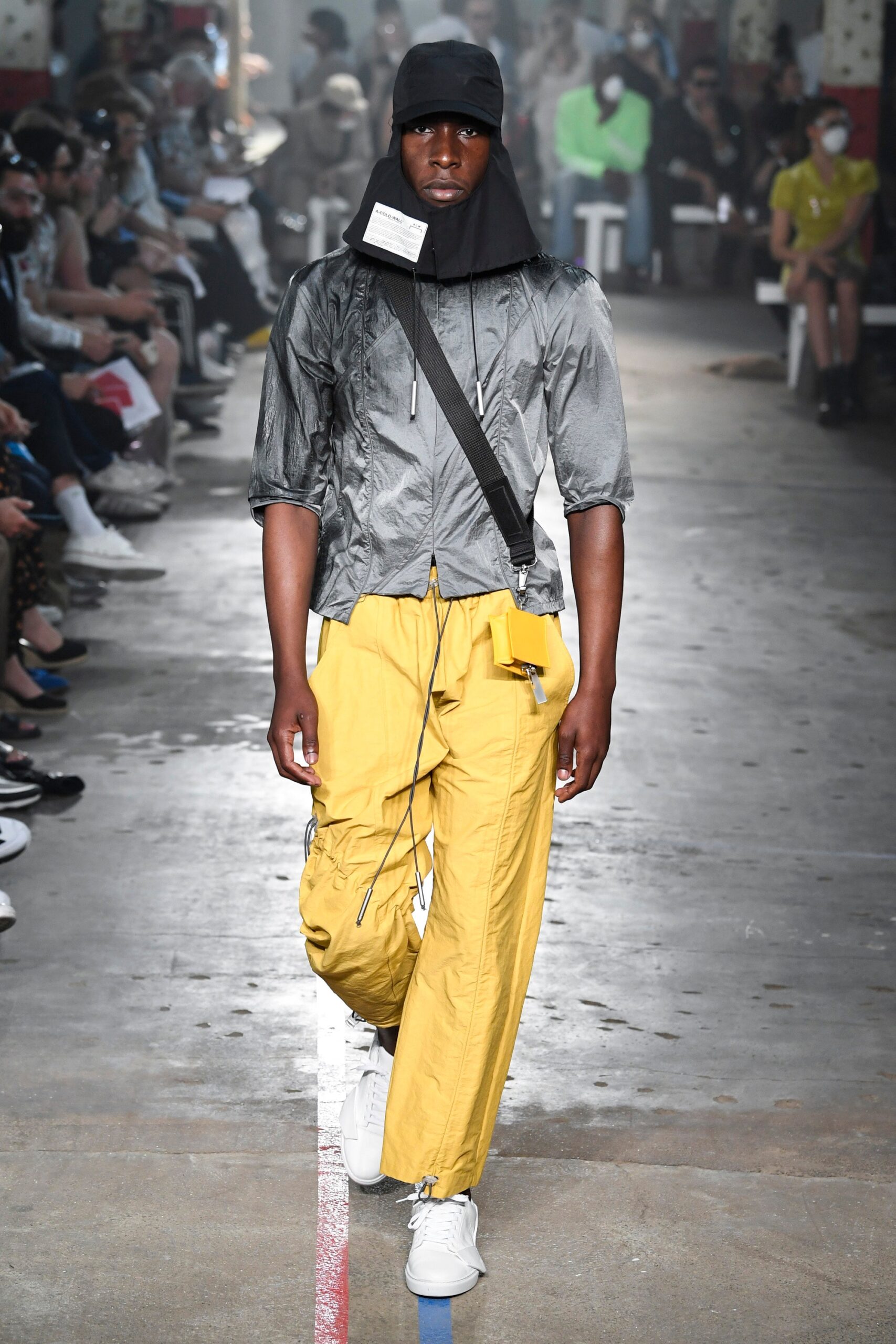 This relaxed-fit jacket in gray nylon features an innovative asymmetric design with a collared neckline and zippered details. Paired with vibrant yellow pants, the ensemble creates a striking contrast that emphasizes both functionality and urban style.