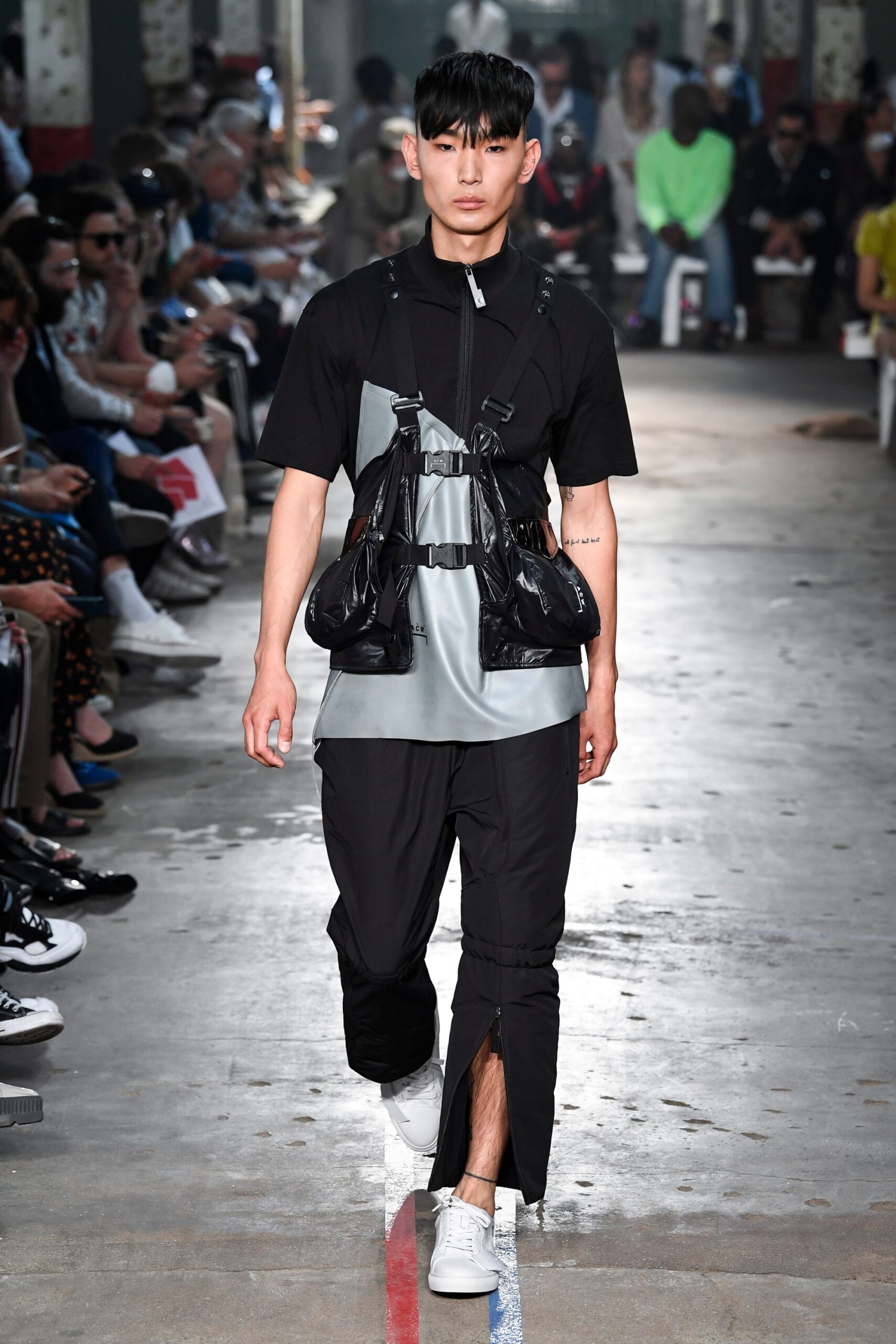 This ensemble features a relaxed top in black and gray, characterized by an asymmetric design and a zippered detail that adds a contemporary edge. Paired with matching pants, the look embodies an urban aesthetic, blending functionality with modern style.