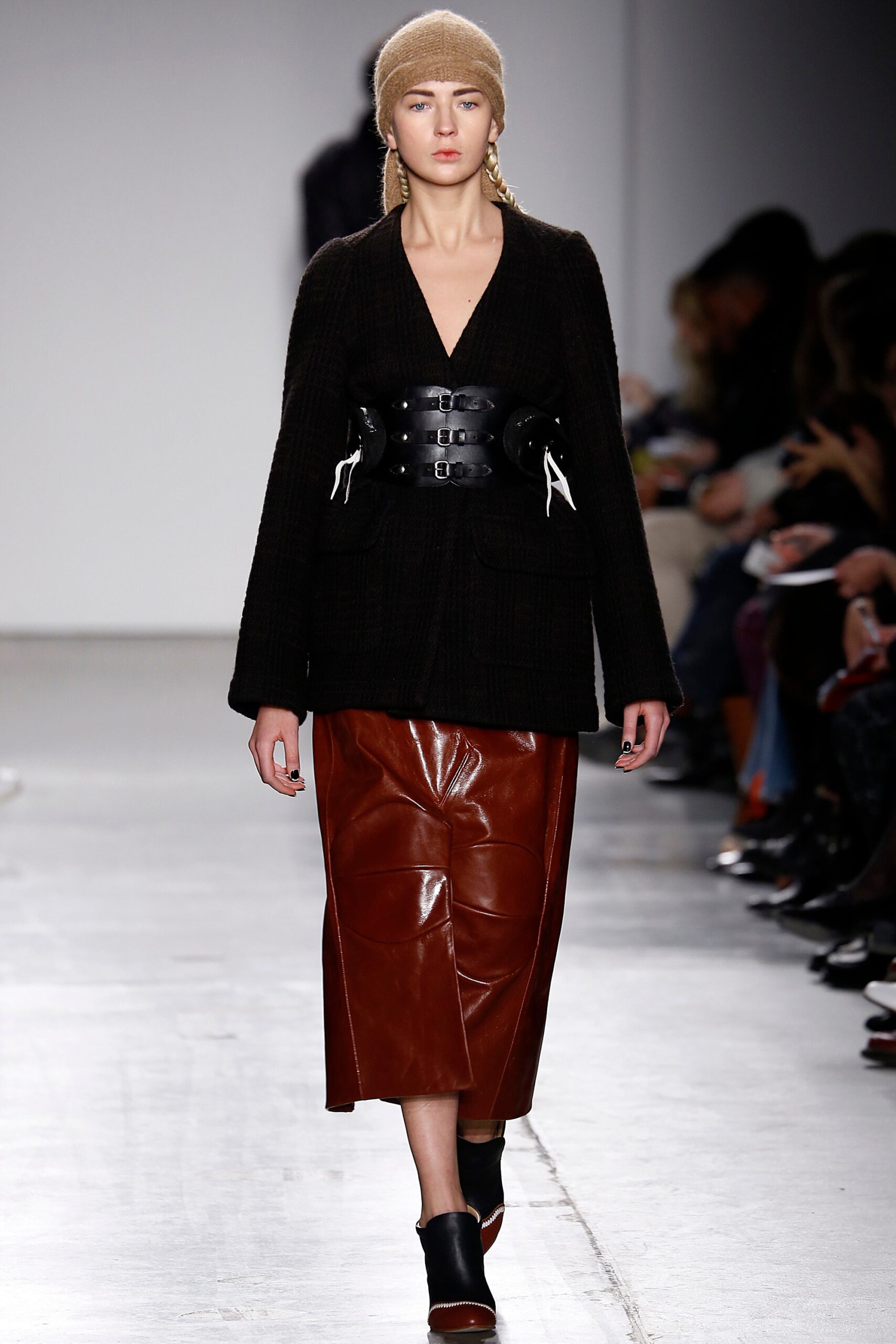 A fitted black jacket with a collared neckline paired with a brown leather skirt featuring an asymmetric design.