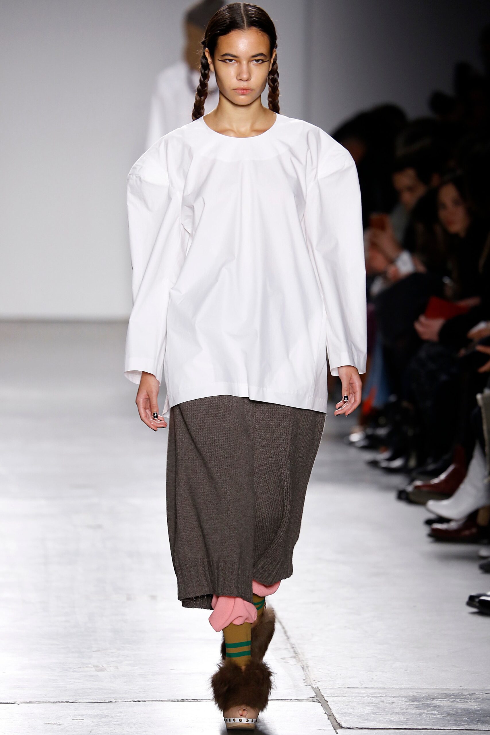 A relaxed fit white long-sleeve top paired with a pleated gray skirt.