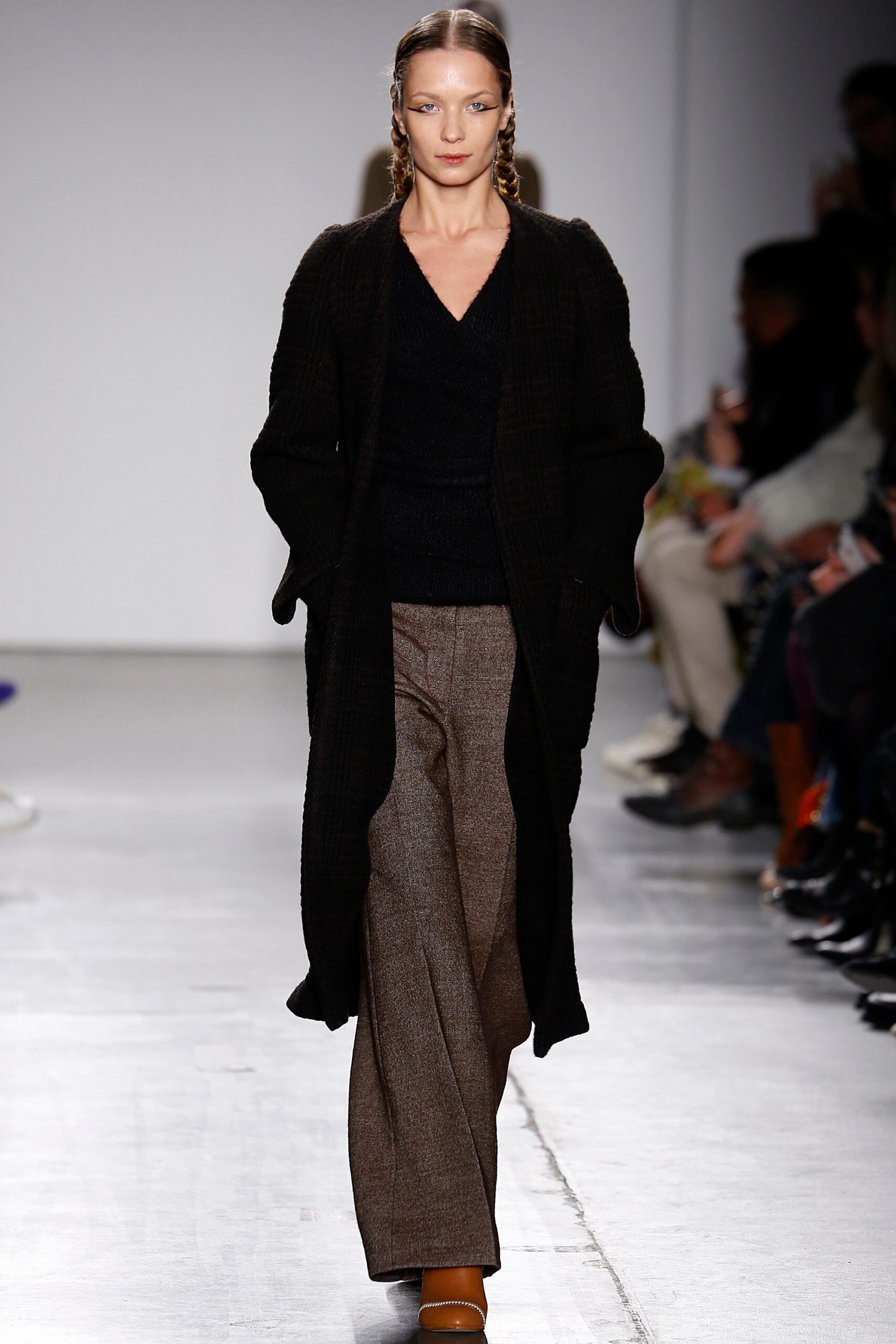 A relaxed black wool coat paired with wide-leg brown pants and a V-neck top.
