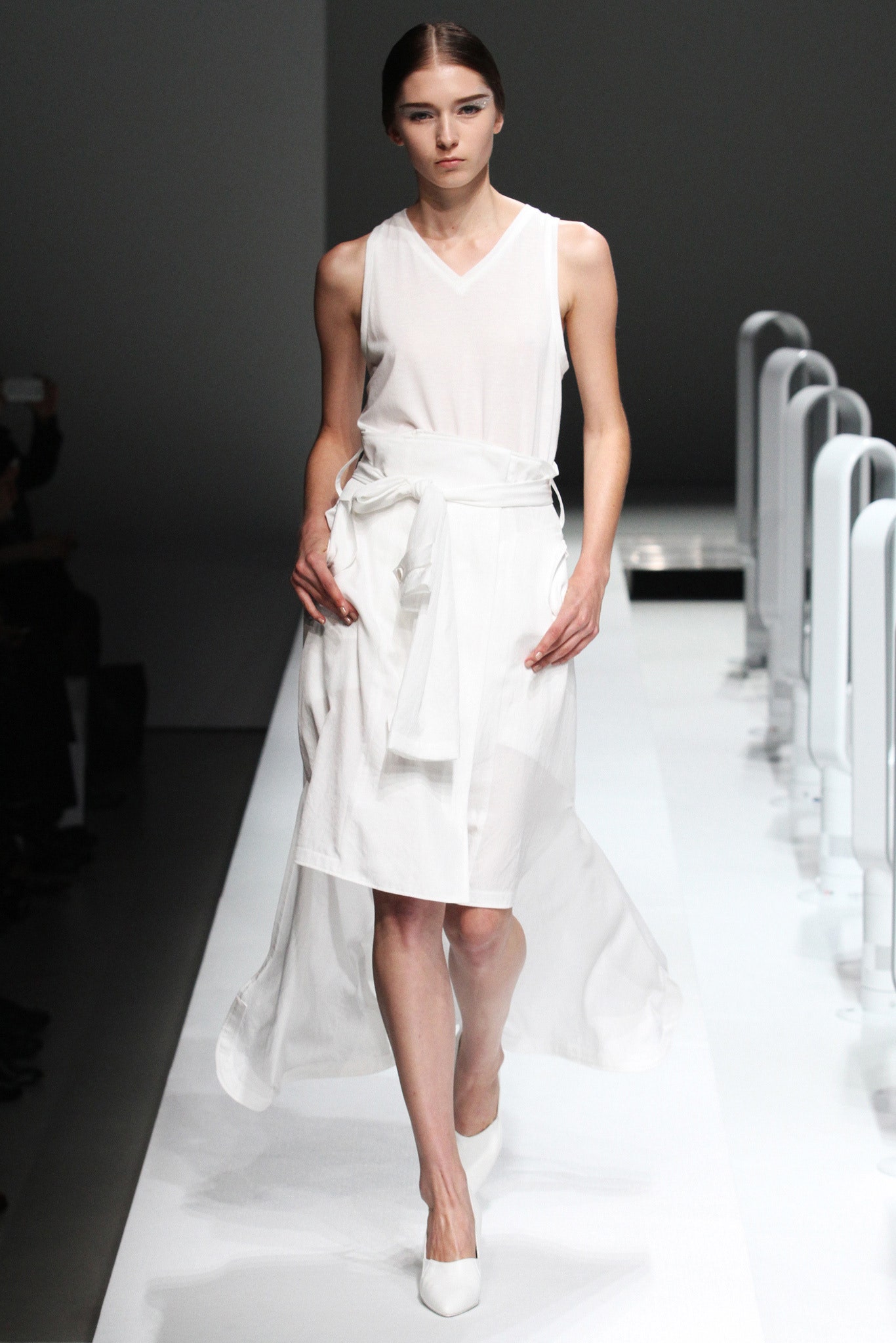 A fitted white sleeveless dress with a V-neckline and asymmetric design.