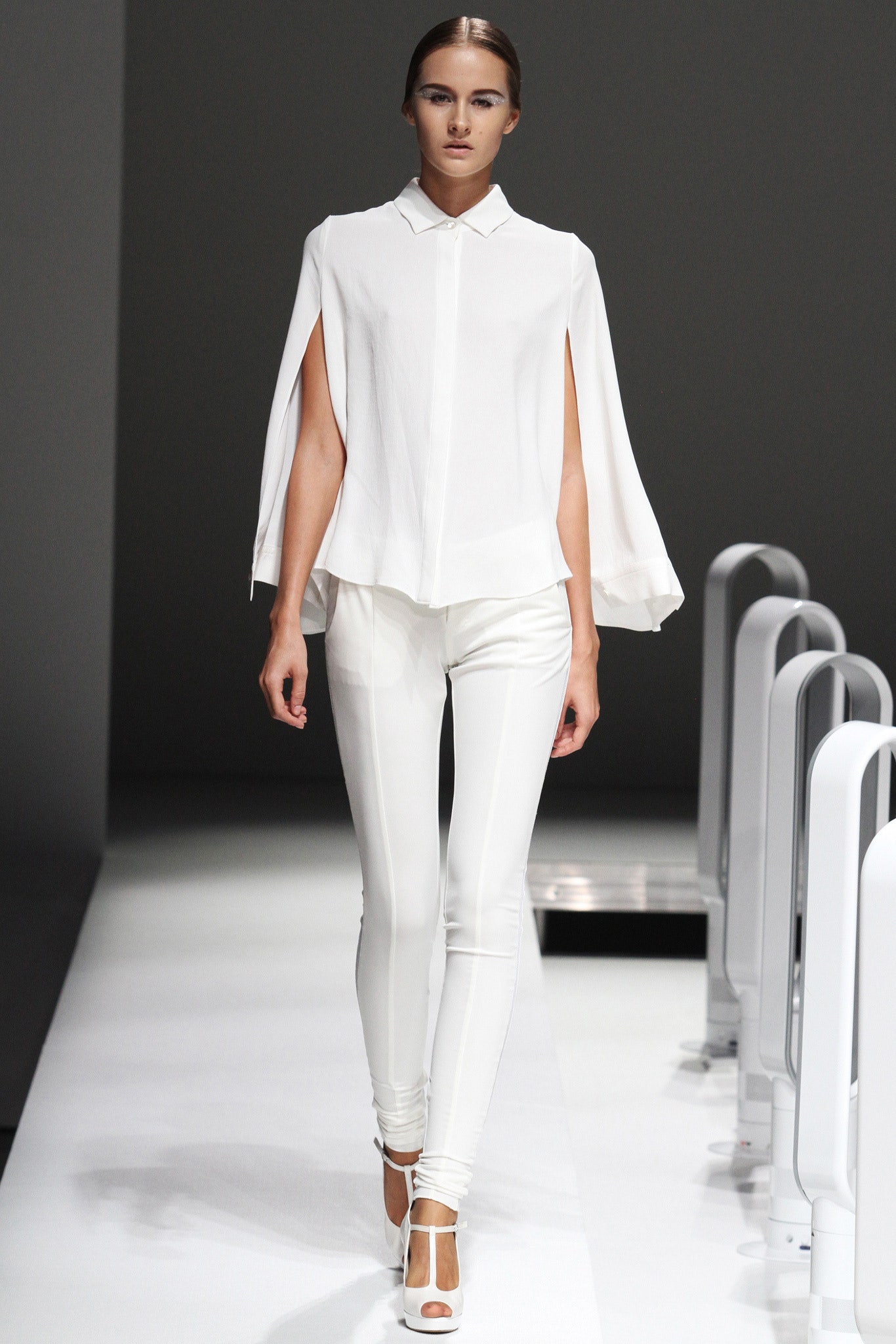 A fitted white blouse with an asymmetric design paired with sleek white pants.