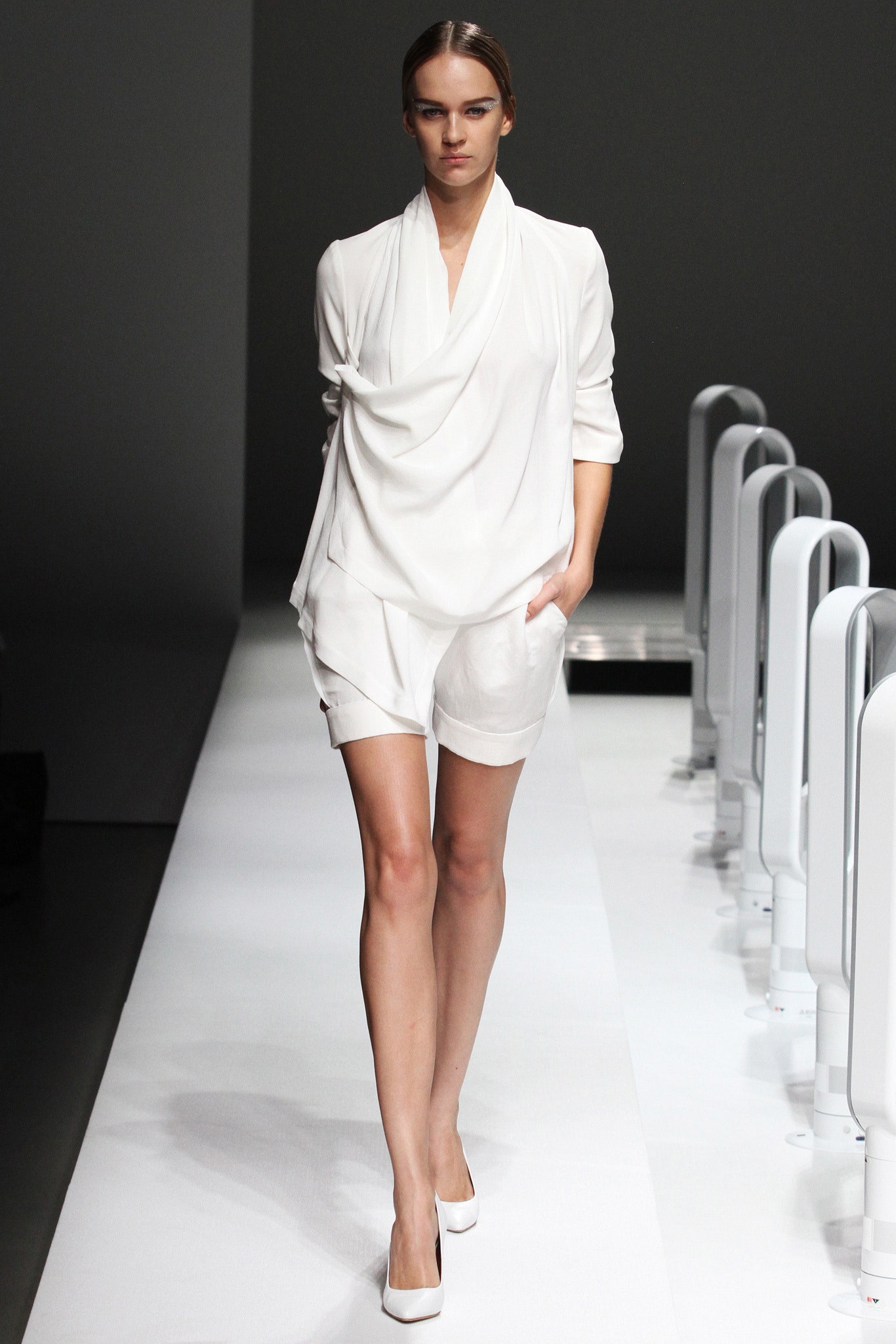 A fitted white jumpsuit with long sleeves and a draped V-neck design.