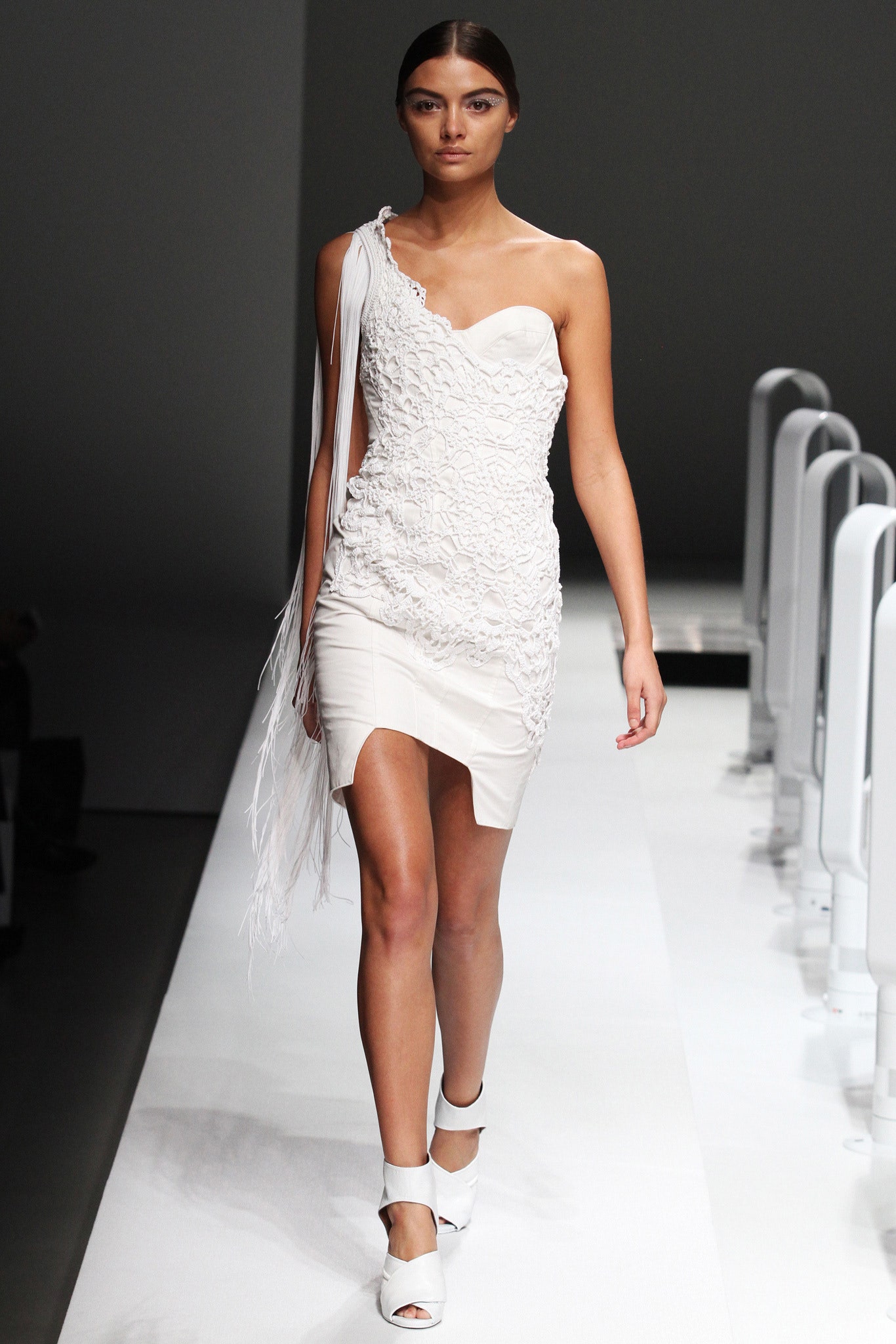 A fitted white silk sleeveless dress with an asymmetric design and ruffled details.