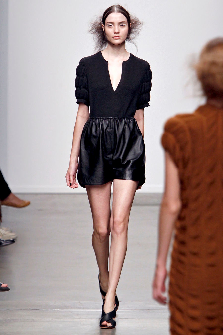 A fitted black leather sleeveless dress with a V-neckline and flared silhouette.
