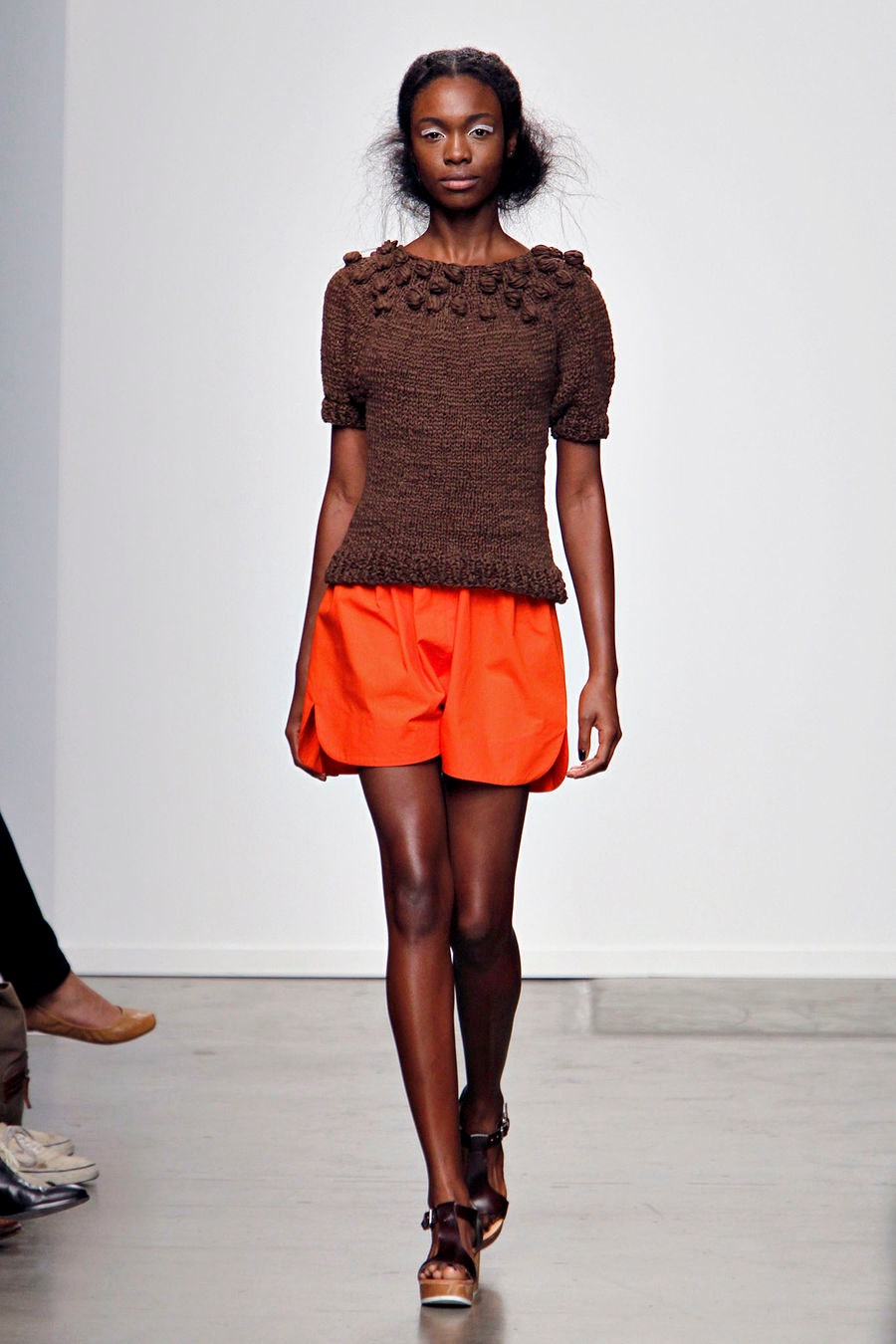 A relaxed brown cotton top with short sleeves paired with pleated orange shorts.