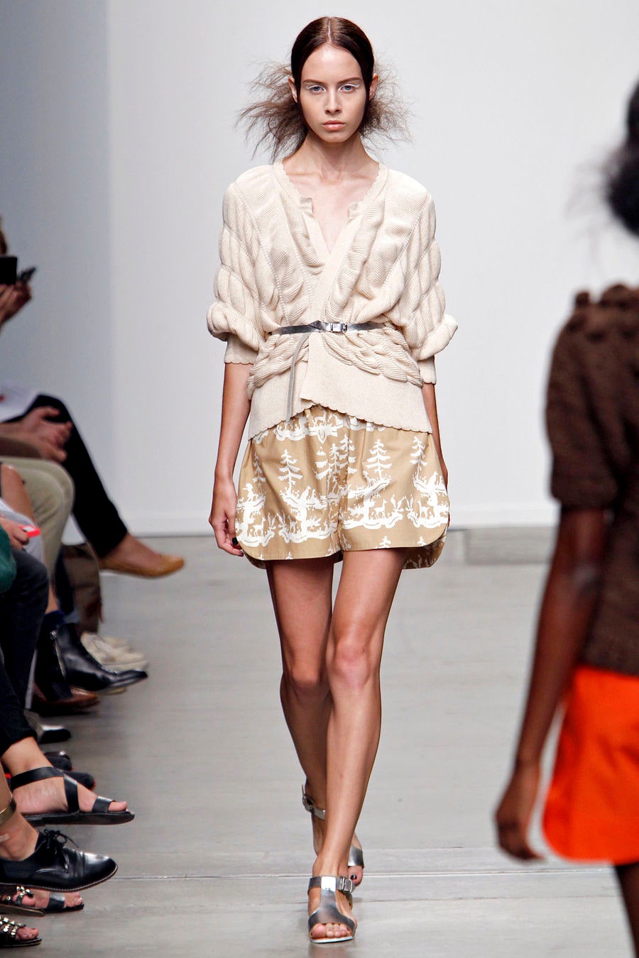 A fitted beige long-sleeve top with a collared design paired with a pleated gold skirt featuring embroidery.