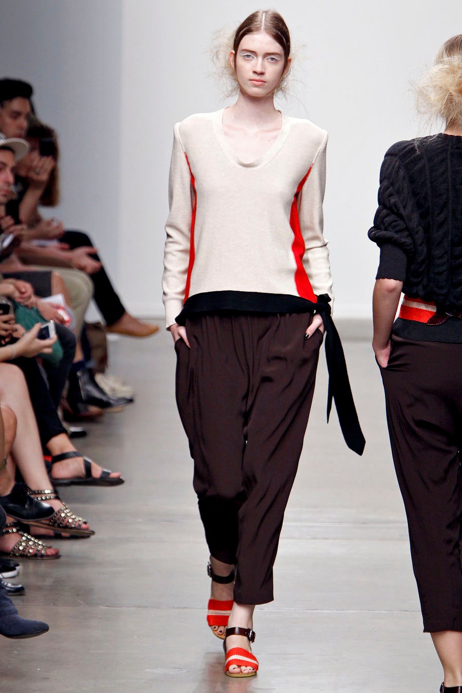 A relaxed beige long-sleeve top with color-blocked details paired with black pleated pants.
