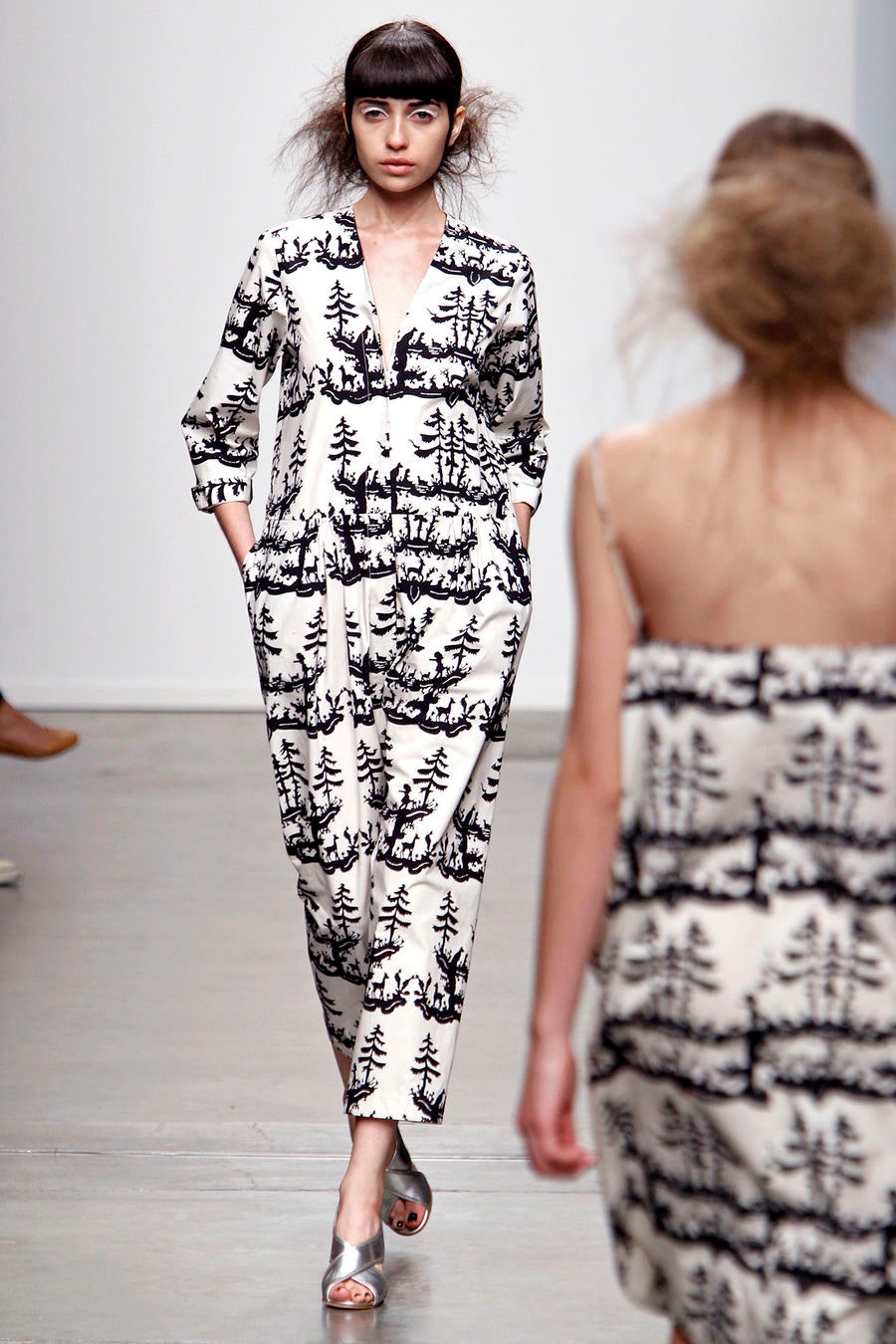 A relaxed white jumpsuit with black tree prints and long sleeves featuring a collared neckline.