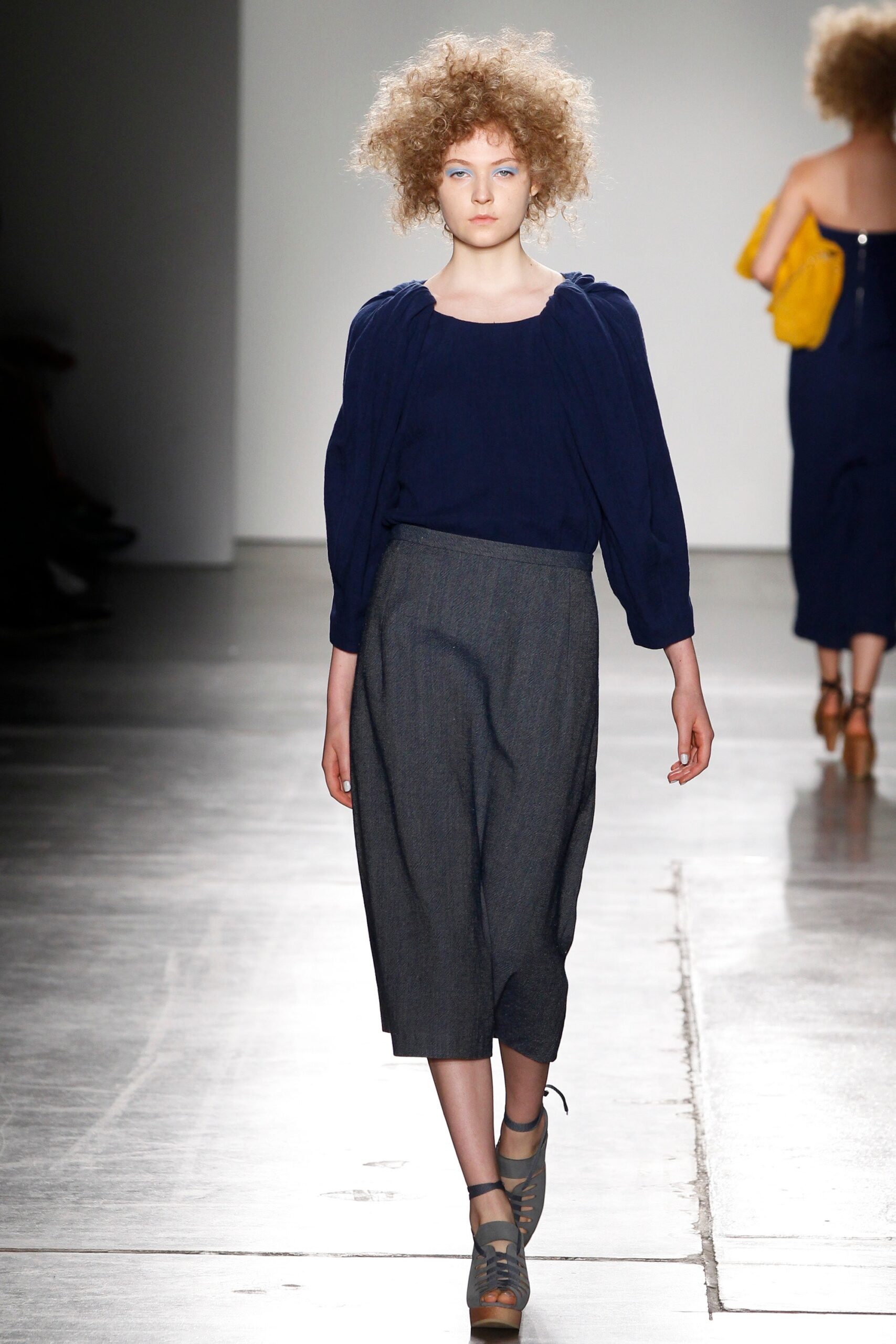 A relaxed blue long-sleeve top paired with pleated gray pants.