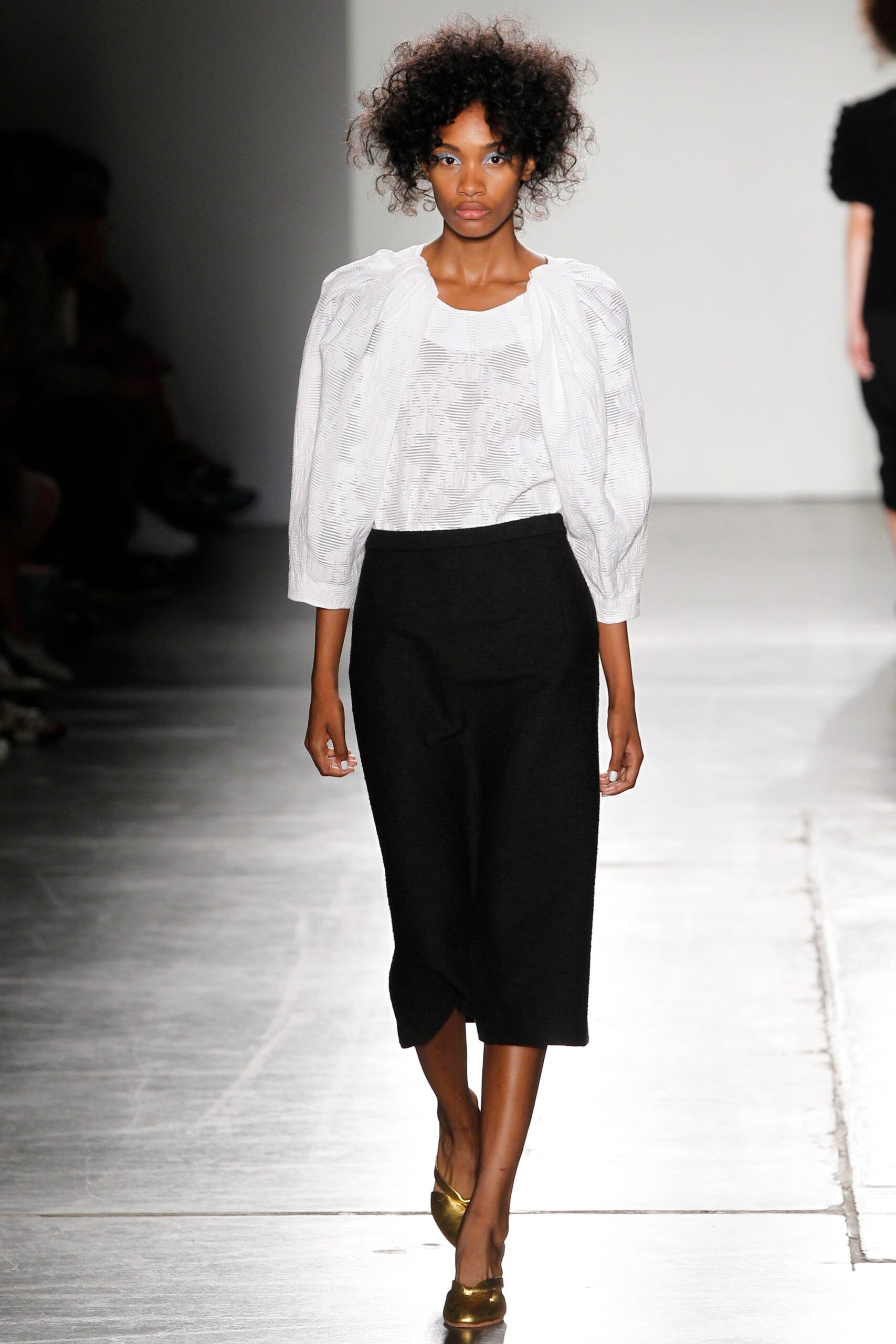 A fitted white cotton blouse with long sleeves paired with a pleated black skirt.