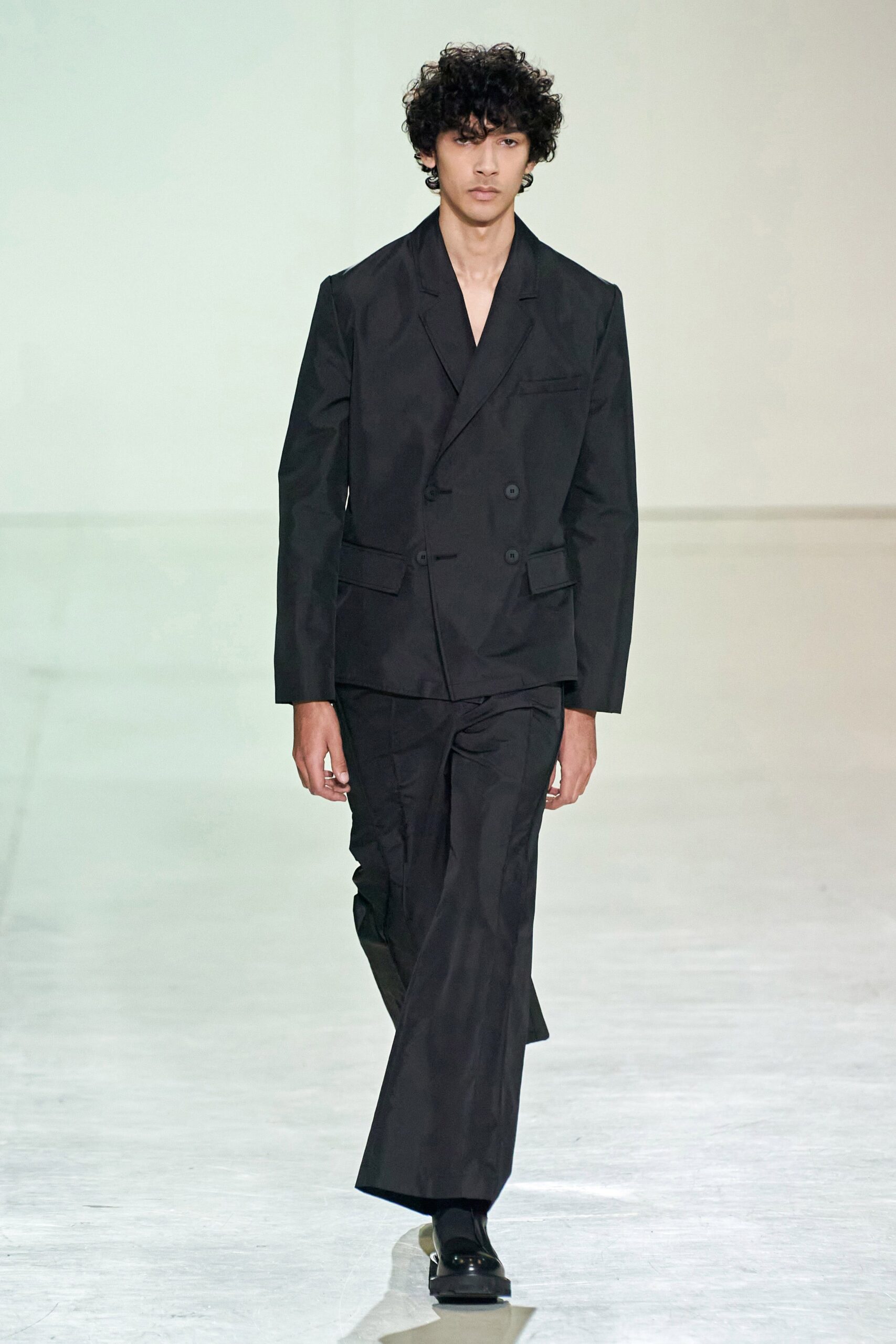A tailored black cotton suit with long sleeves and a collared design, featuring buttoned details.