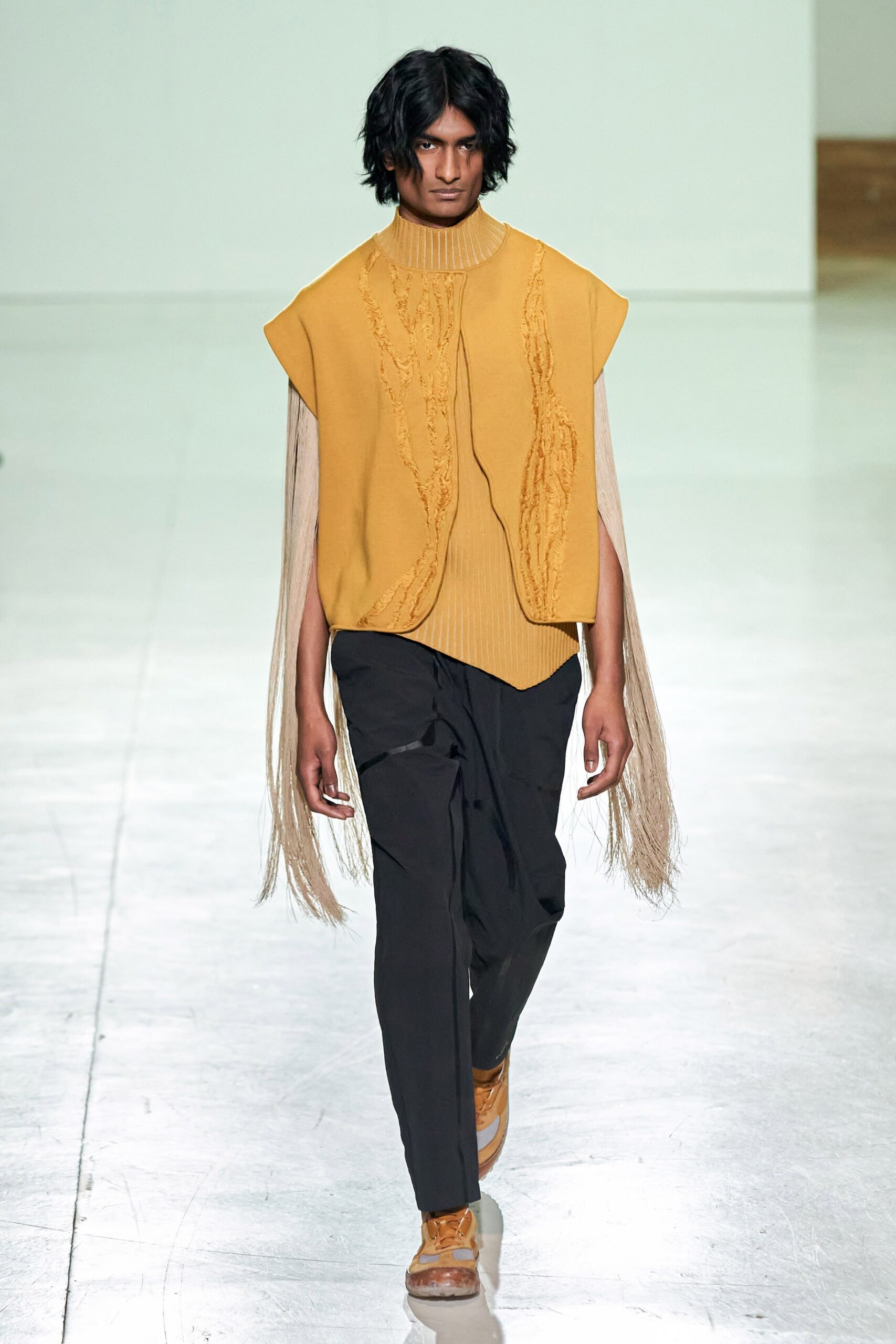 A relaxed yellow sleeveless top with fringed details paired with black pants.