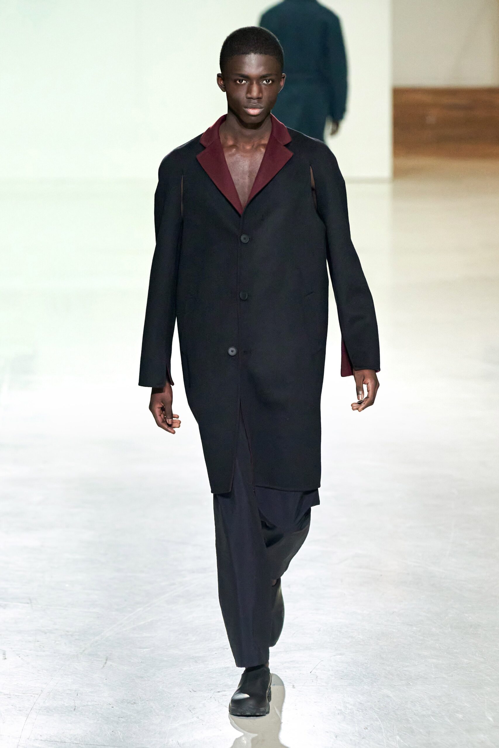 A relaxed black wool coat with long sleeves and an asymmetric design detail.