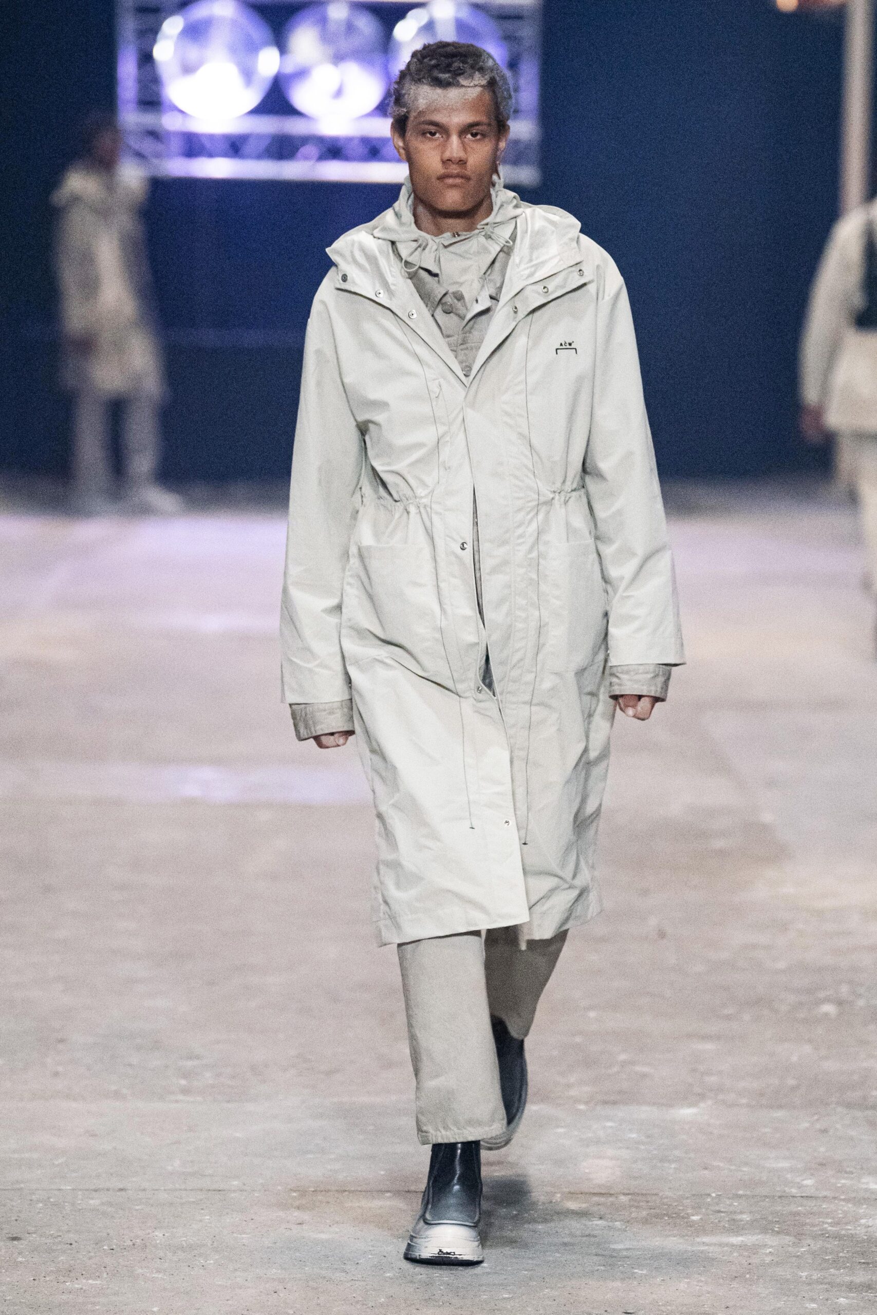 A relaxed beige coat with long sleeves and a collared neckline featuring a zippered closure.