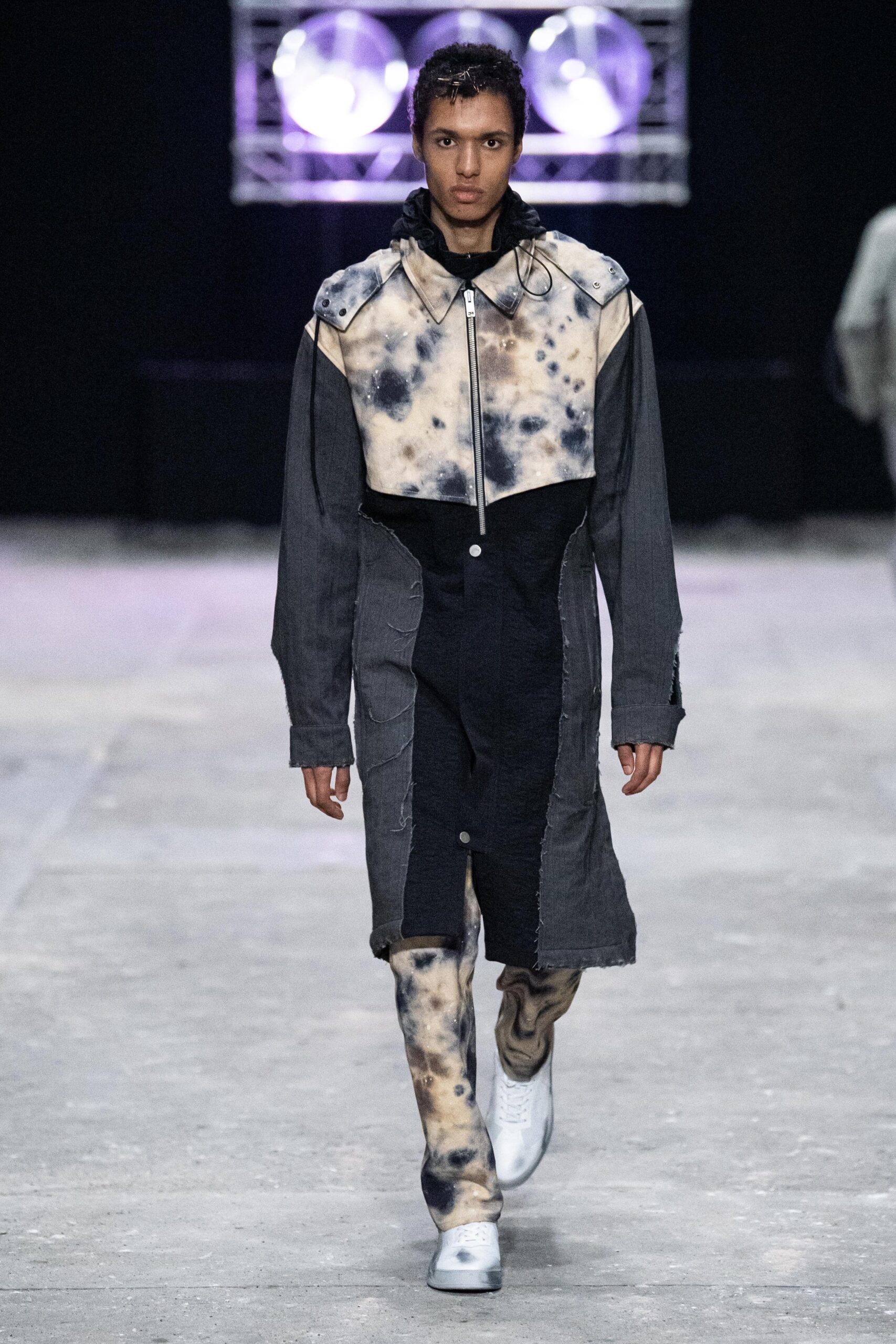 A fitted black and beige denim coat with long sleeves and an asymmetric design, paired with fitted pants.