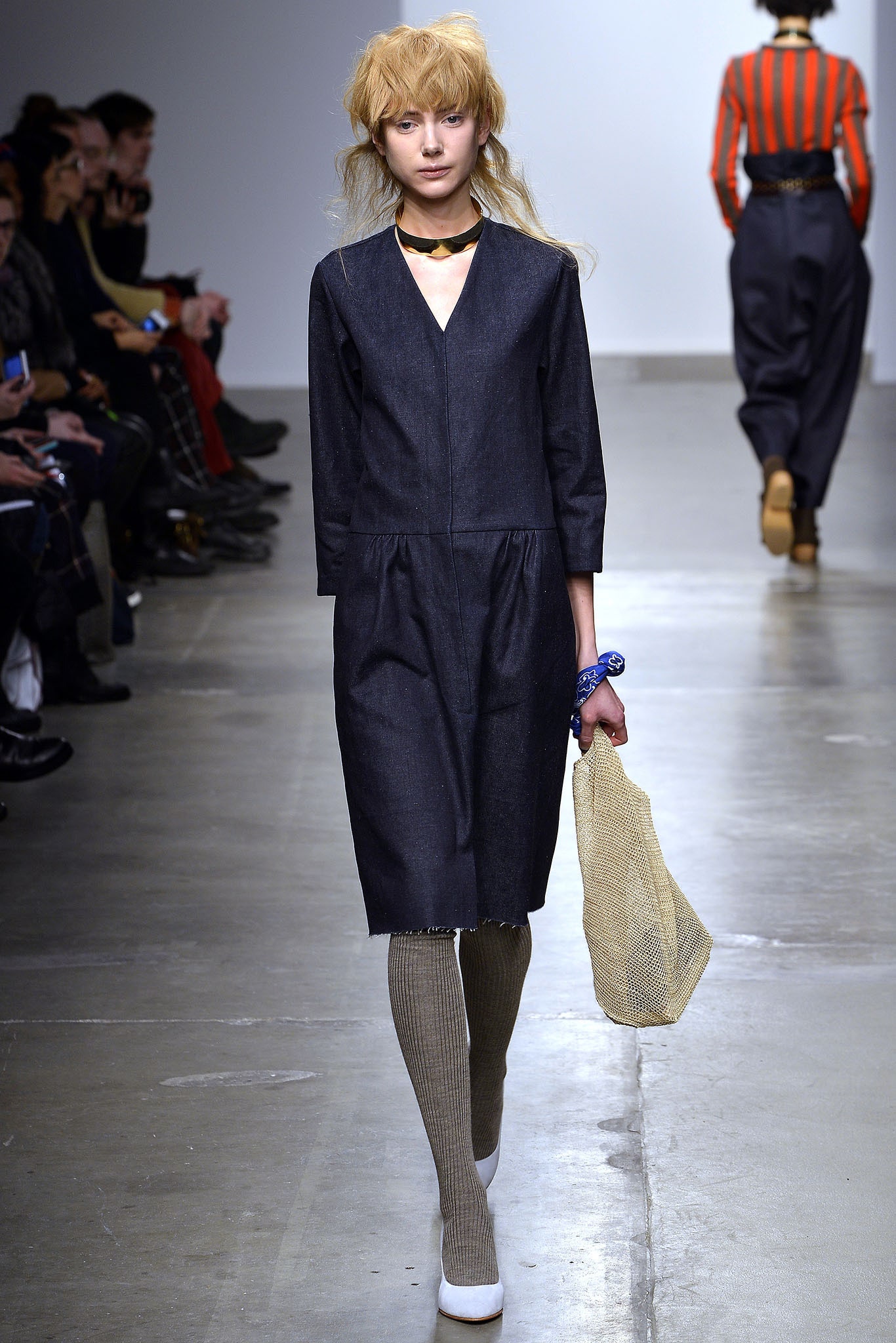 A relaxed blue denim dress with long sleeves and a V-neckline featuring a tiered design.