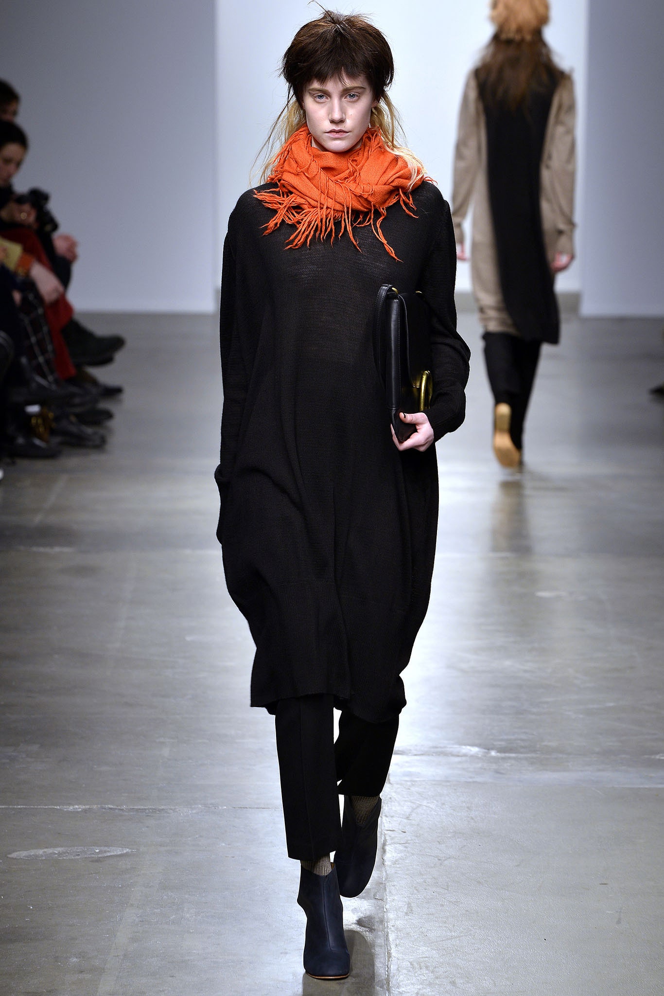 An oversized black dress paired with black pants and an orange scarf for a bold look.