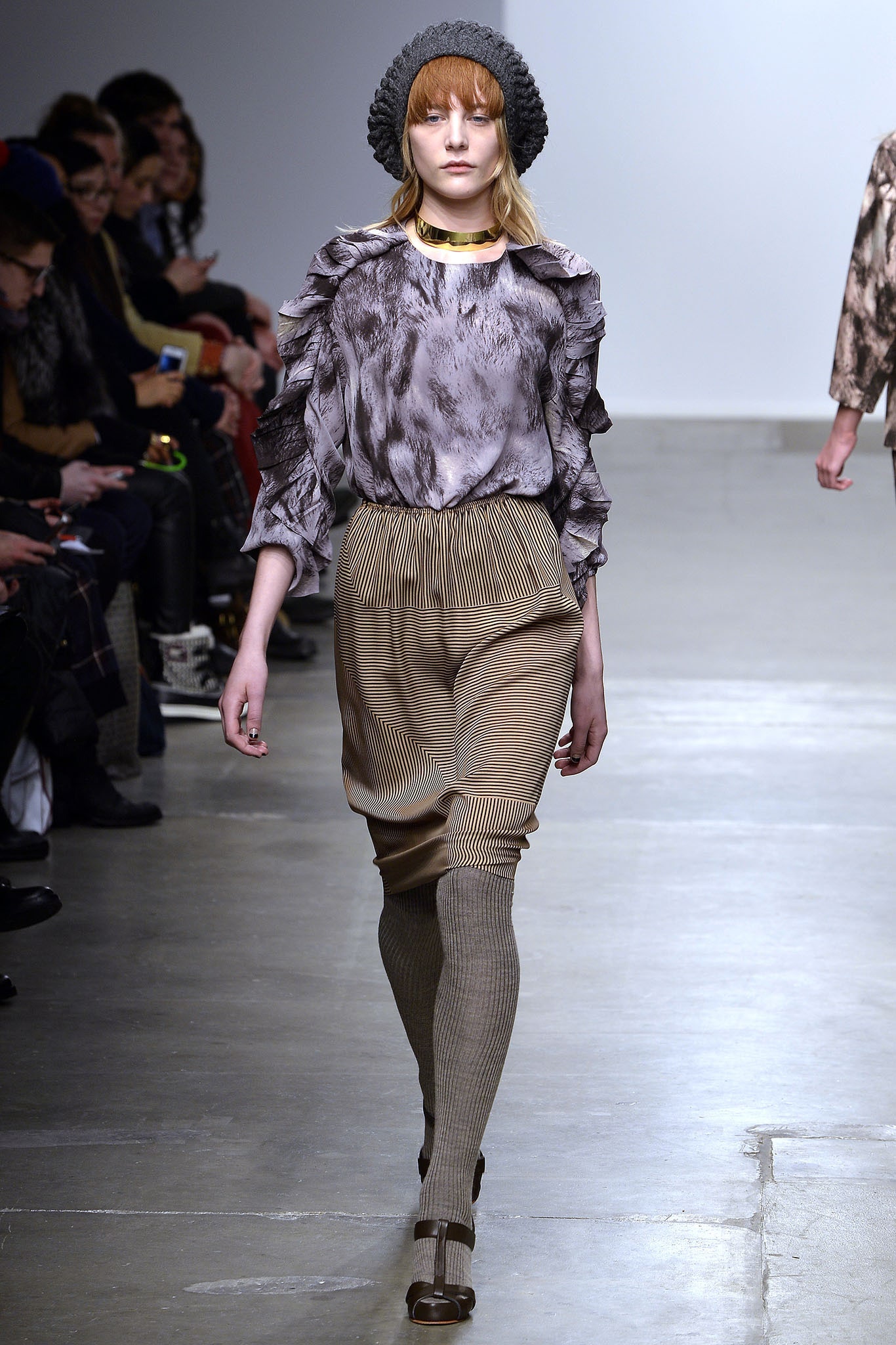A relaxed gray ruffled blouse paired with beige striped pants for a chic runway look.