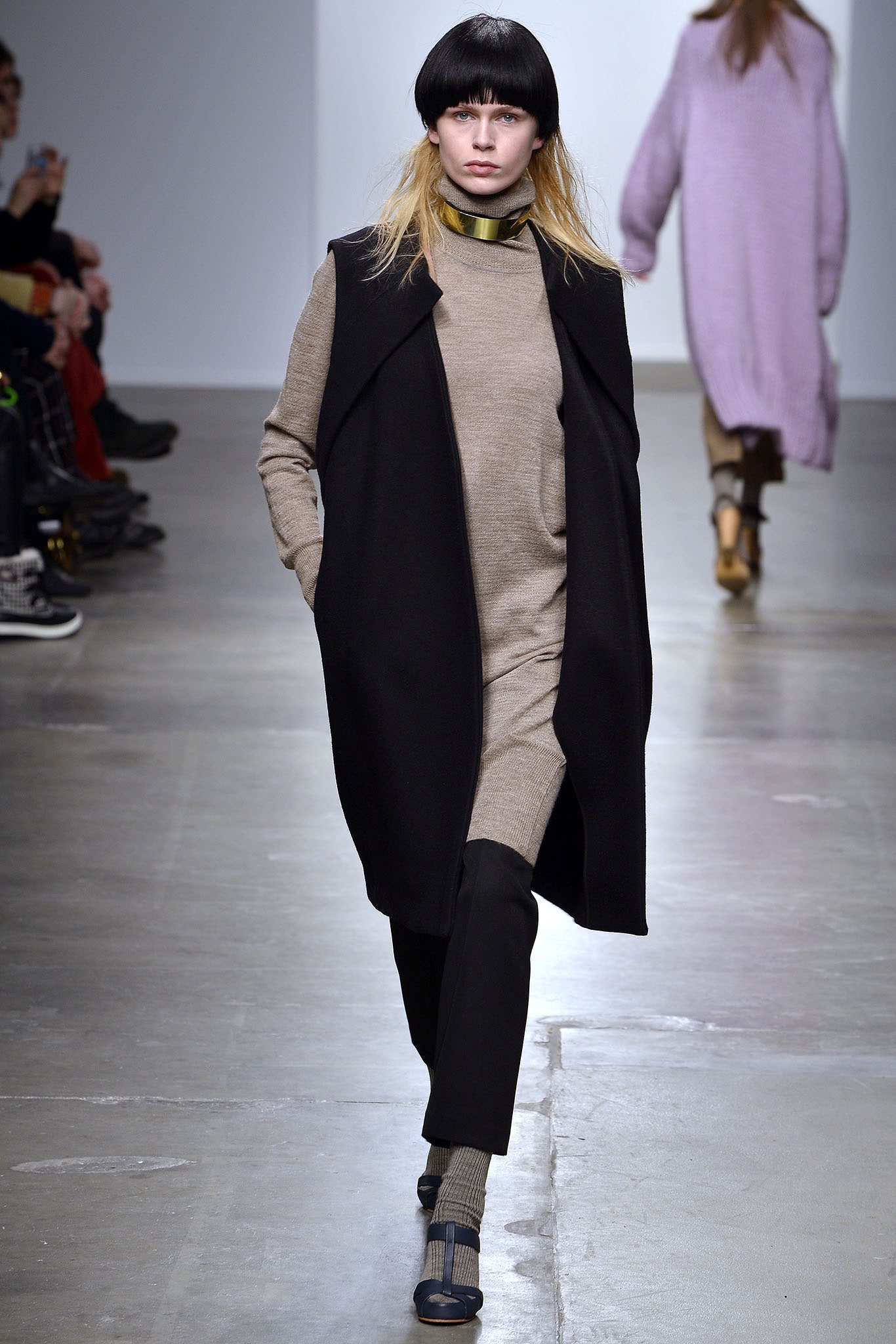 A relaxed black coat layered over a beige sleeveless dress with a V-neckline.