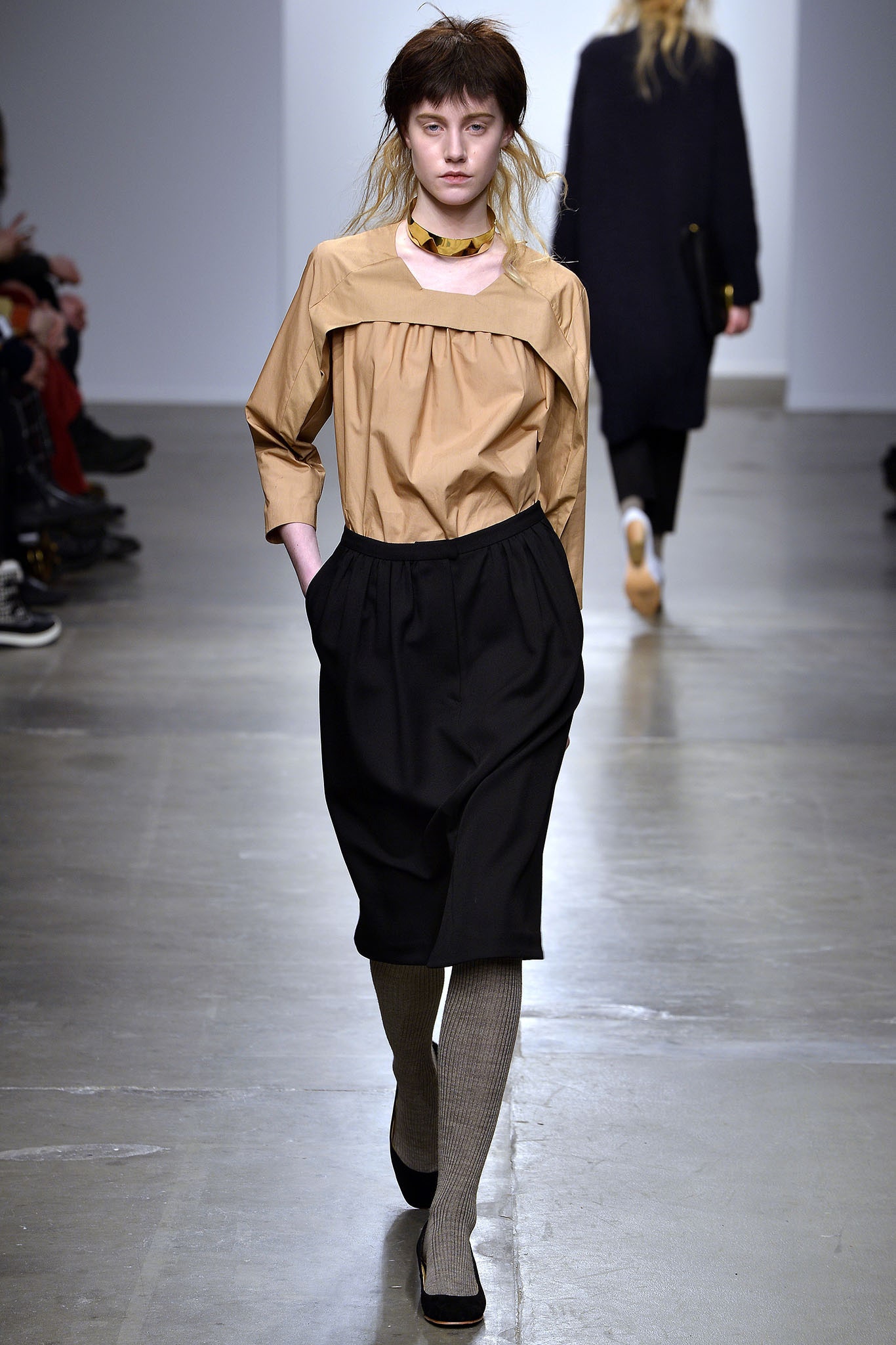 A relaxed beige cotton blouse with long sleeves paired with a pleated black skirt.