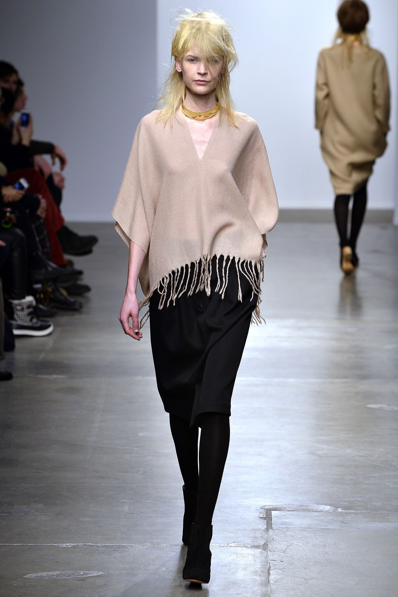 A relaxed beige wool poncho with fringed edges paired with a black skirt.