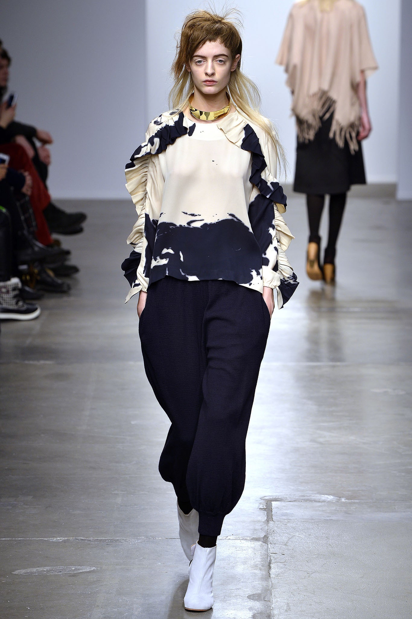 A relaxed cream top with ruffles and a print, paired with black relaxed-fit pants.