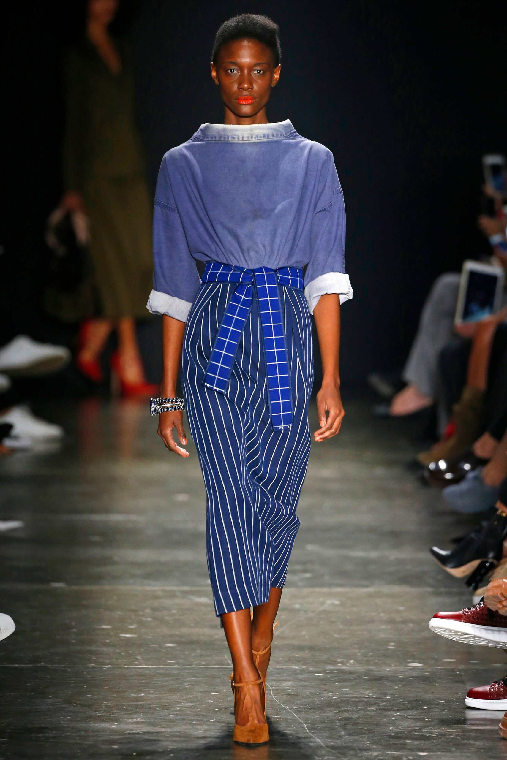 A relaxed blue cotton shirt with a collared neckline paired with a belted striped skirt.