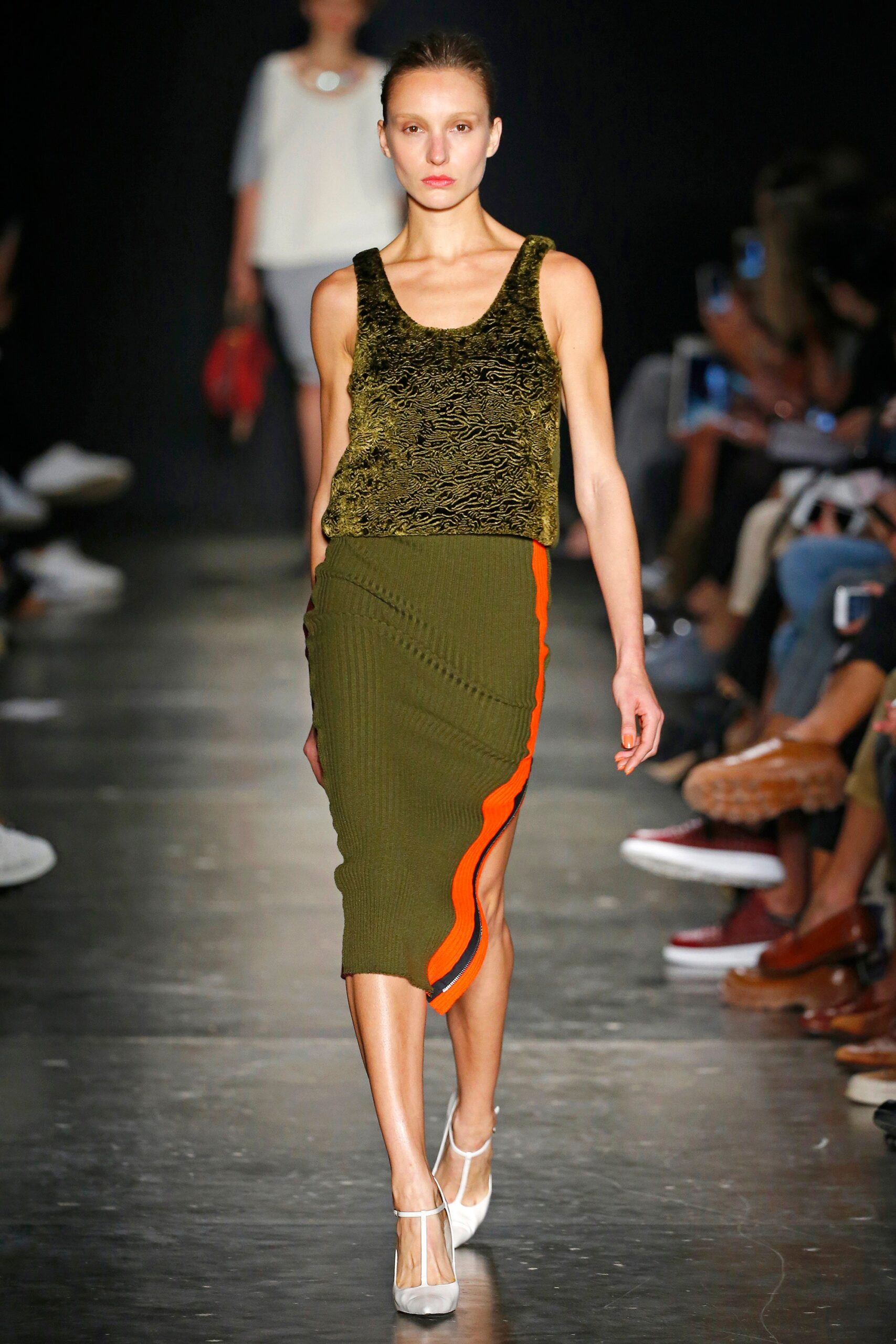 A fitted sleeveless green knit top paired with a fitted asymmetric skirt featuring orange detailing.