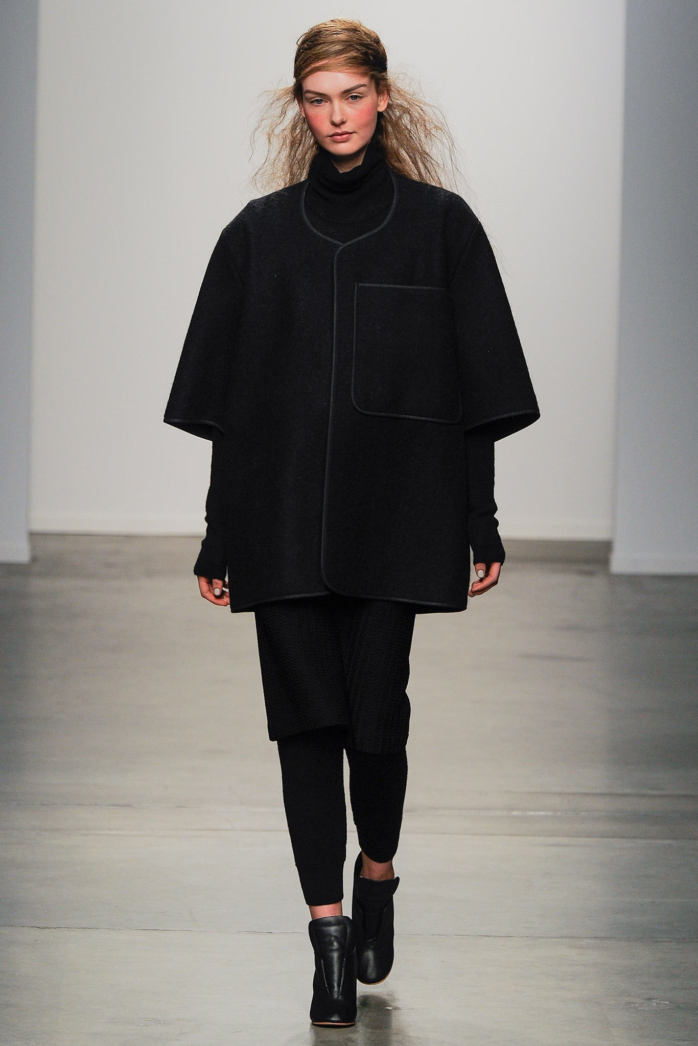 A relaxed black wool coat with long sleeves and an asymmetric design paired with black pants.