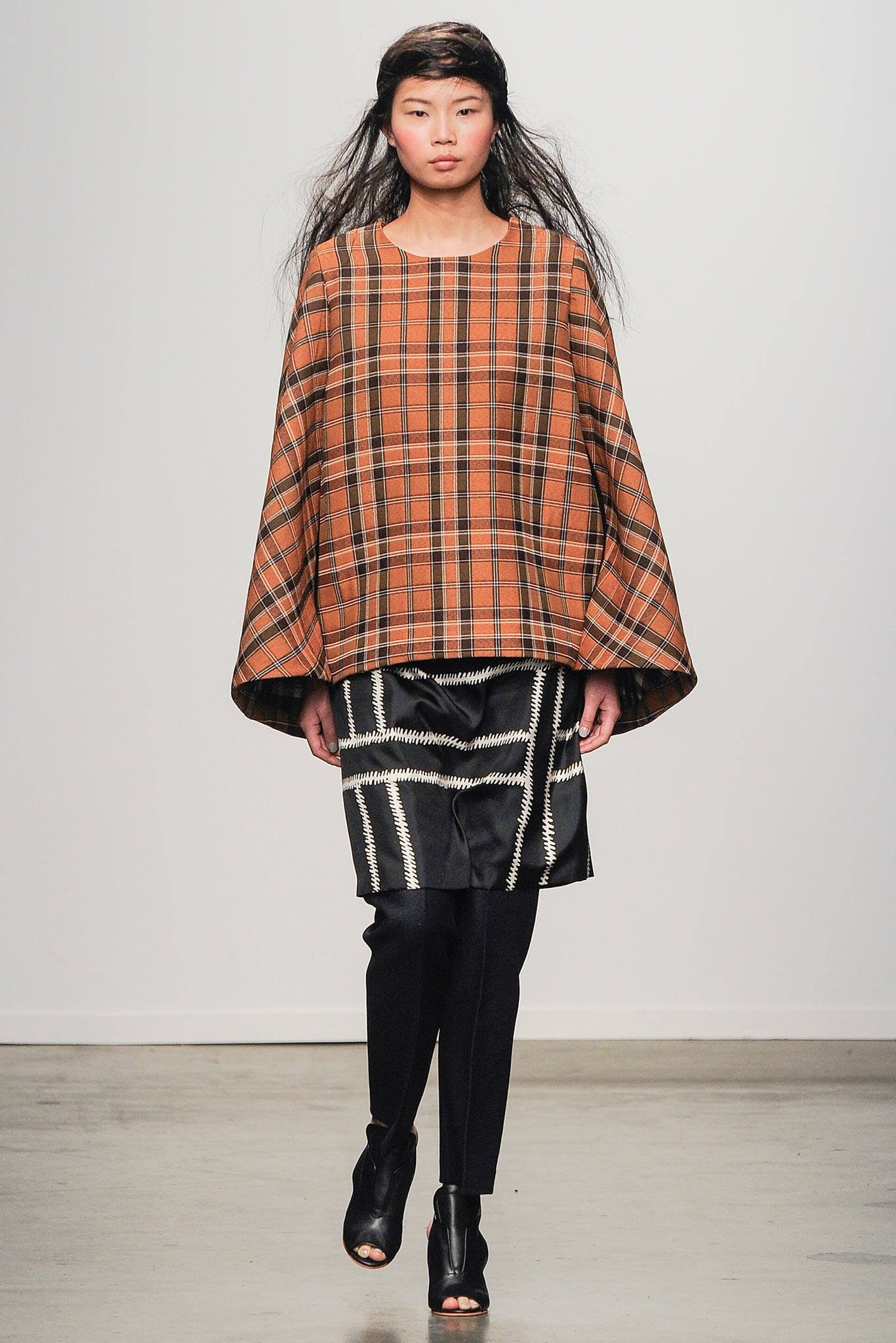 A relaxed orange checked top with long sleeves layered over a black skirt.