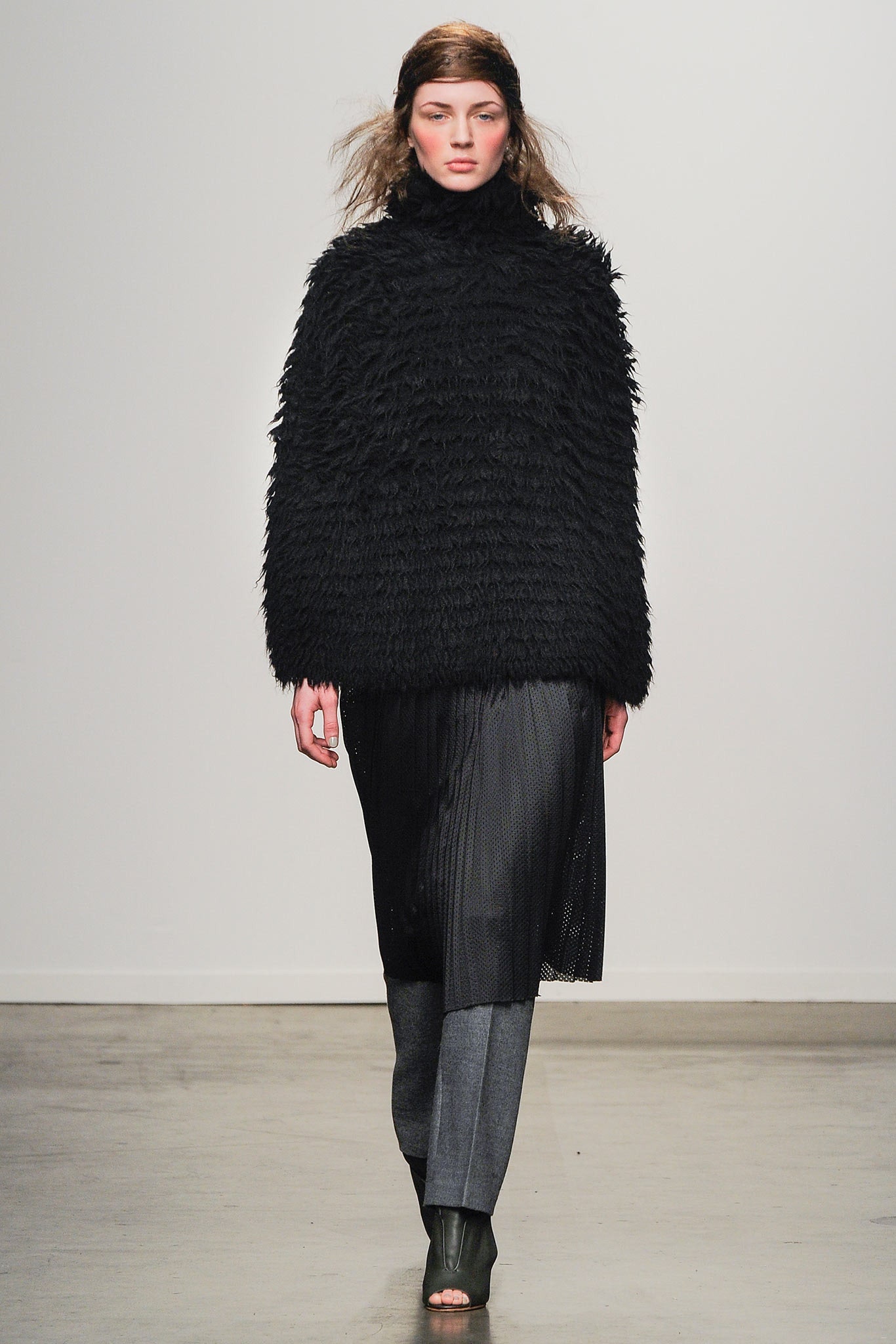 An oversized black wool coat with long sleeves and a high neckline, layered over a skirt.