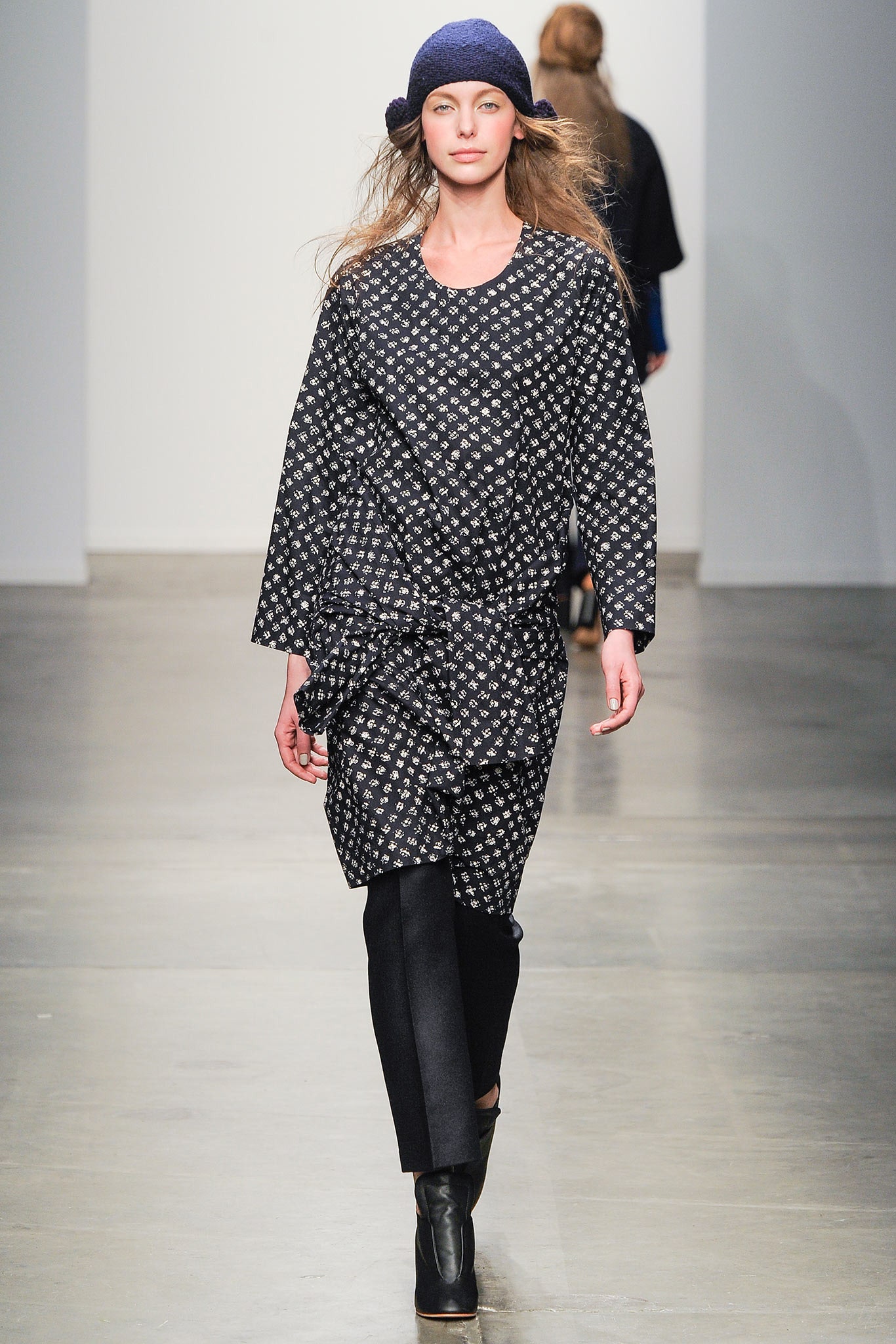 A relaxed black and white printed dress with long sleeves and an asymmetric design paired with pants.
