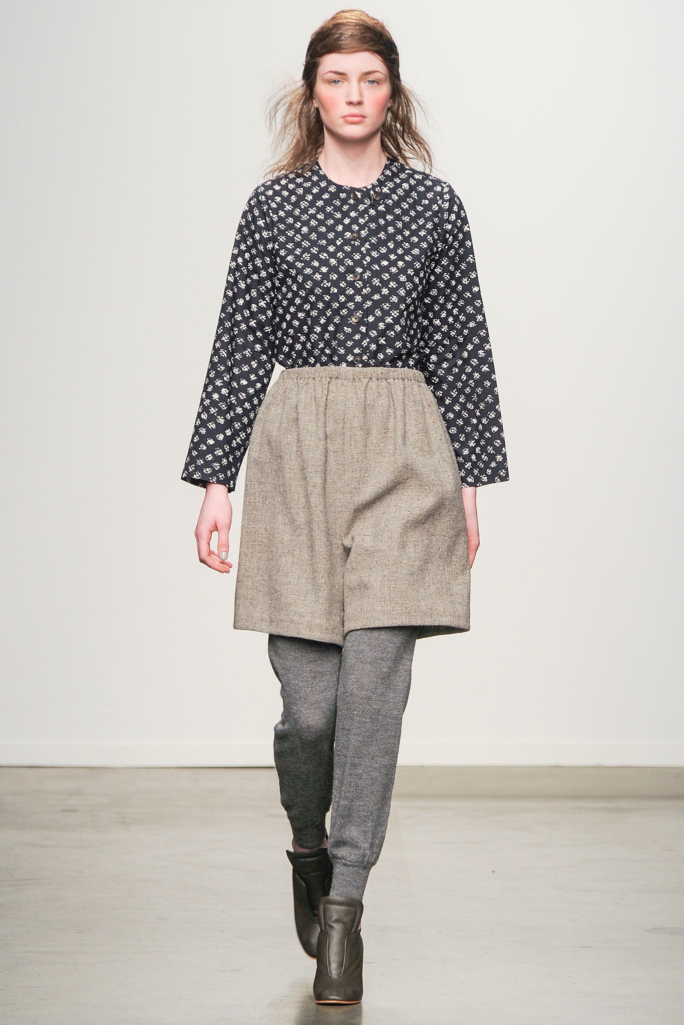 A relaxed black printed blouse paired with pleated gray shorts for a stylish look.