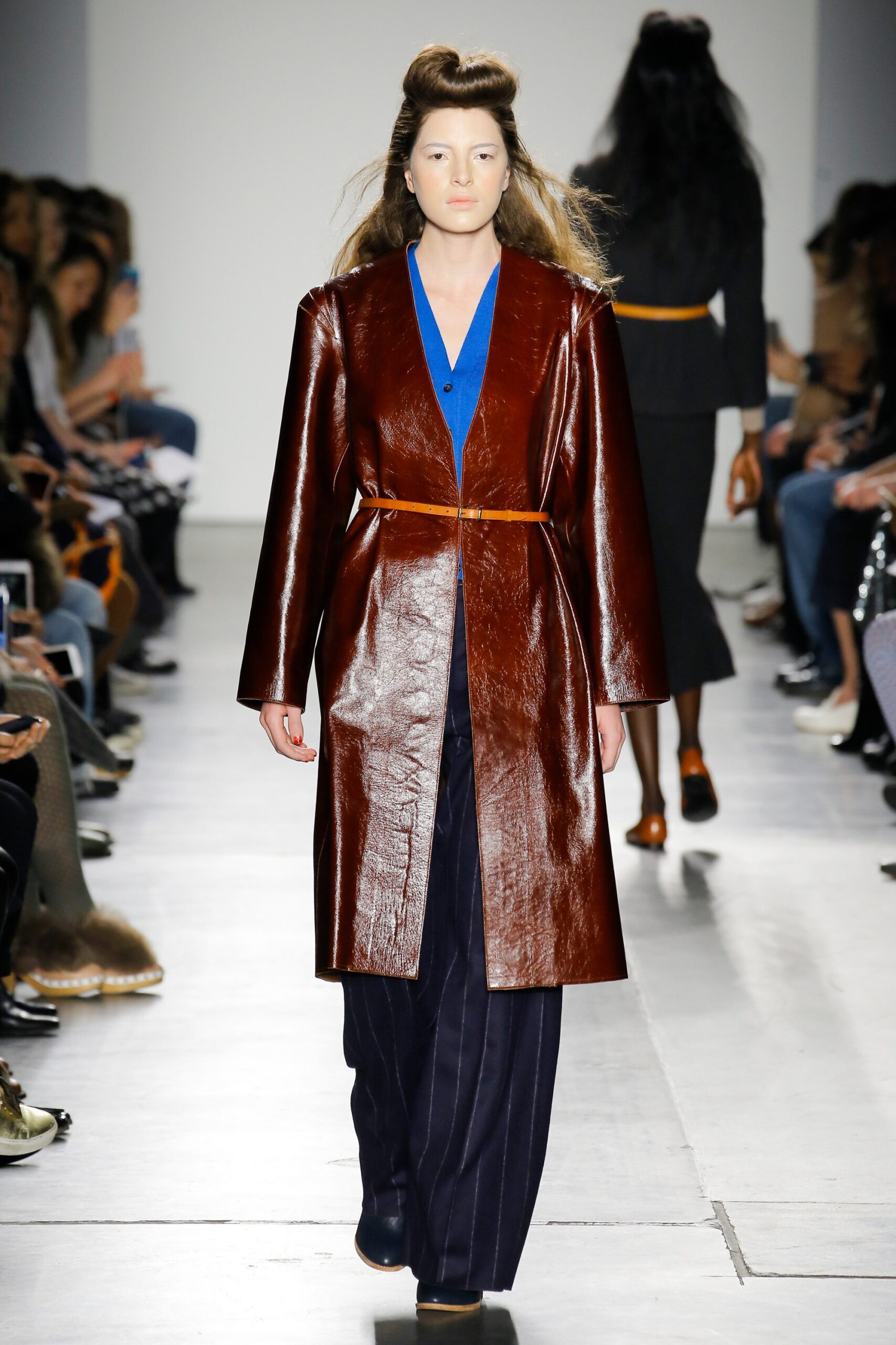 A relaxed brown leather coat paired with a blue collared shirt and striped pants.