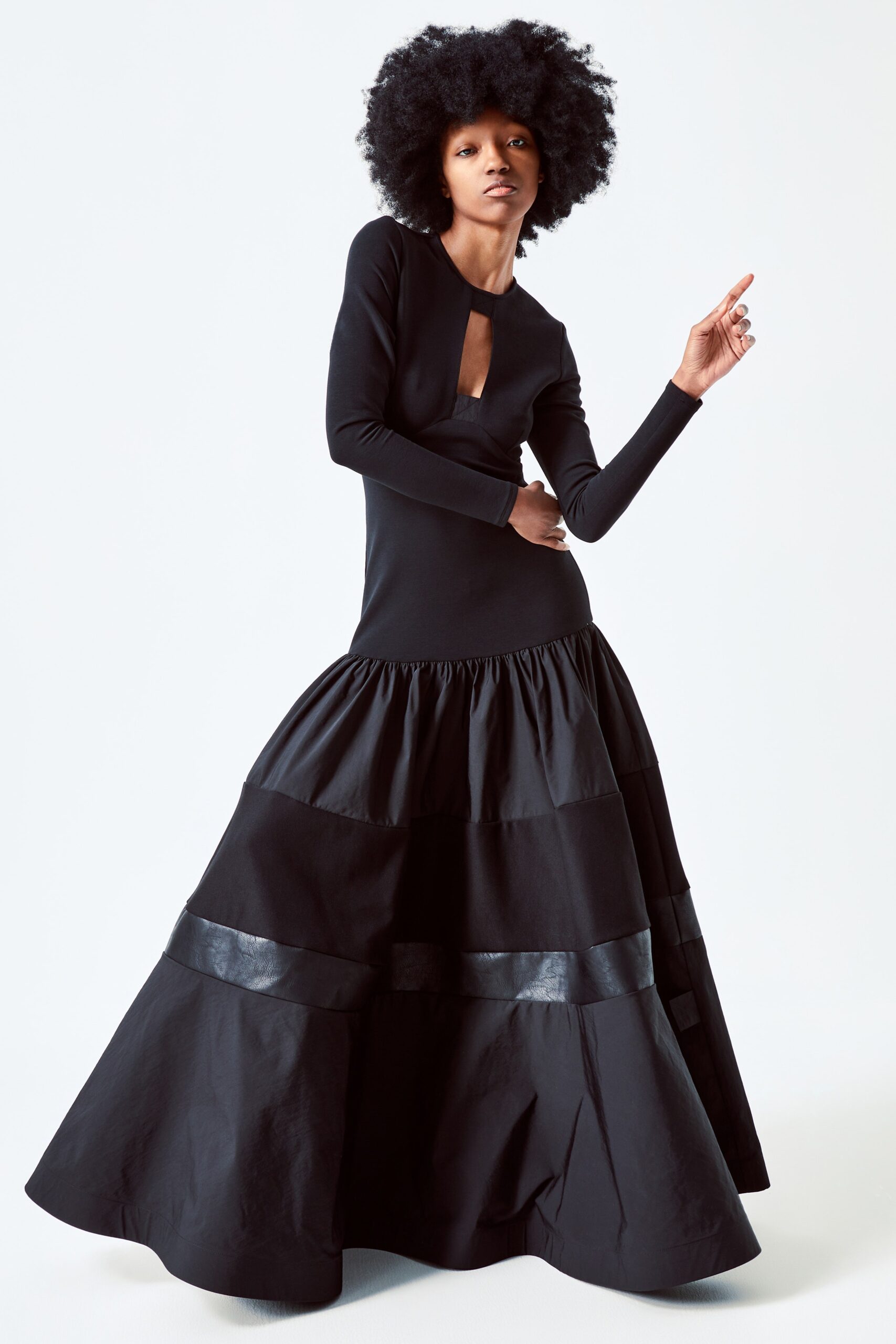 This dress features a fitted bodice with long sleeves and a high neckline, flowing into a dramatic tiered skirt. The interplay of textures and the structured silhouette create a striking visual impact, emphasizing movement and form.