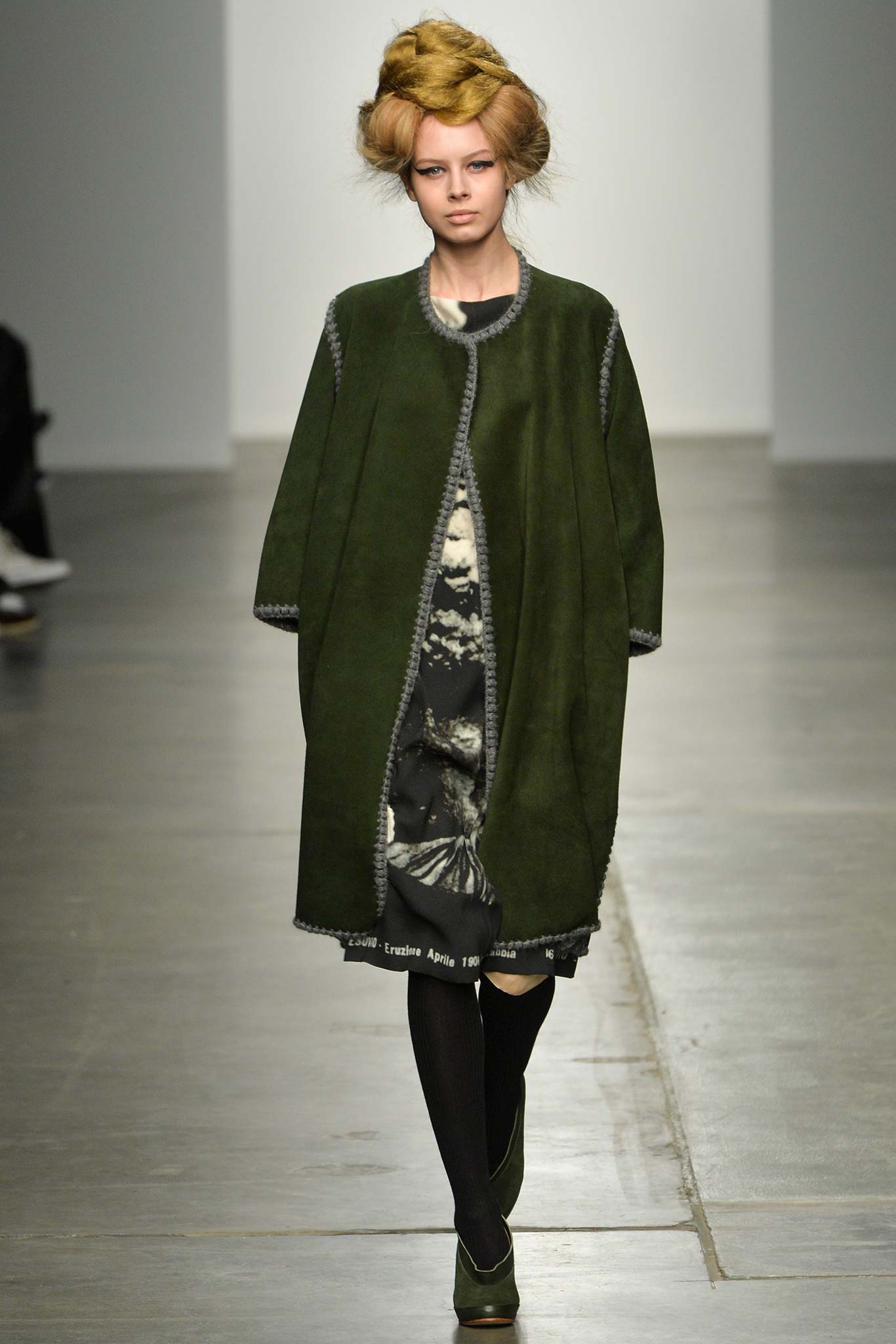 A relaxed green wool coat with long sleeves layered over a black dress.