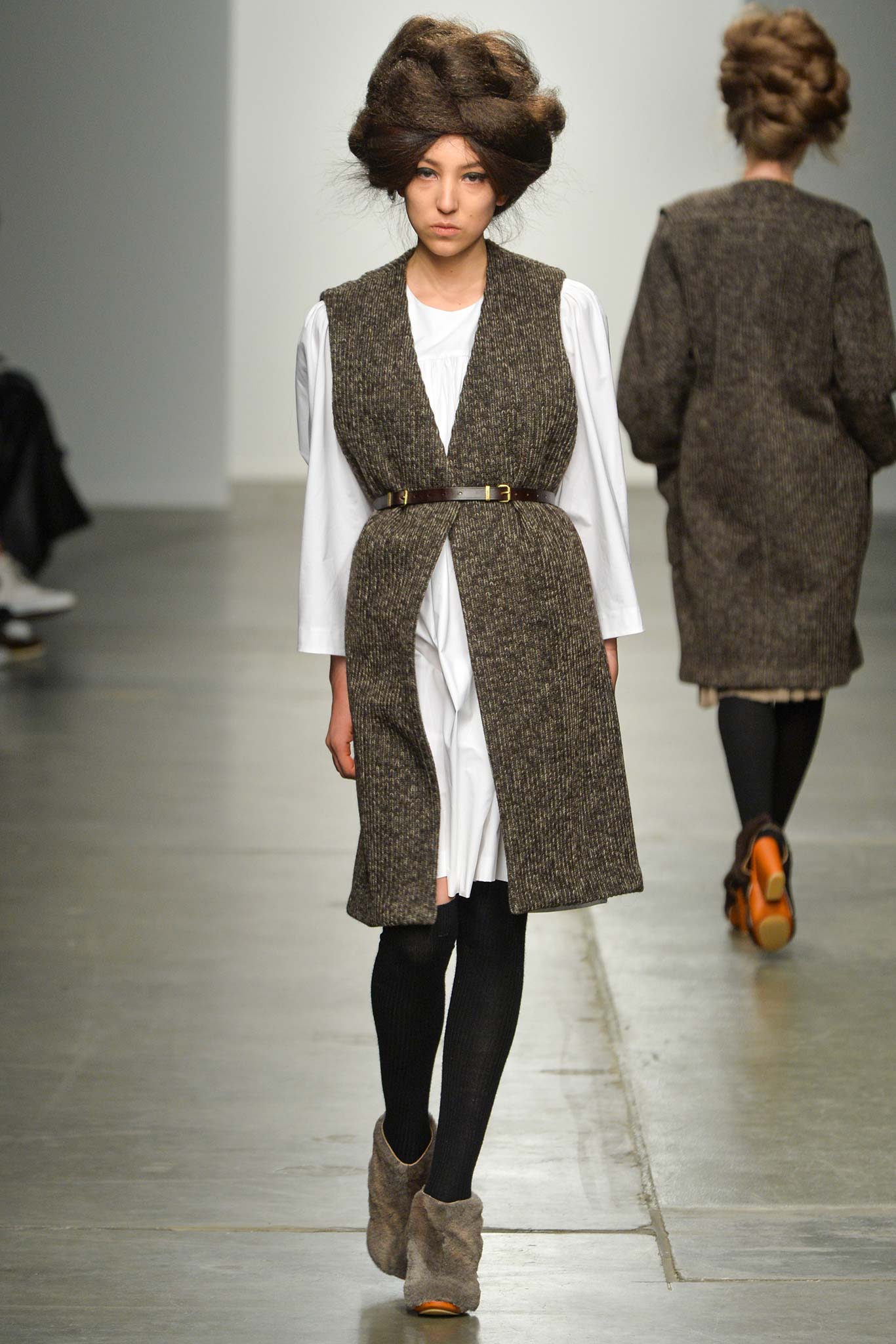 A fitted brown wool coat layered over a white dress with long sleeves and a belted waist.