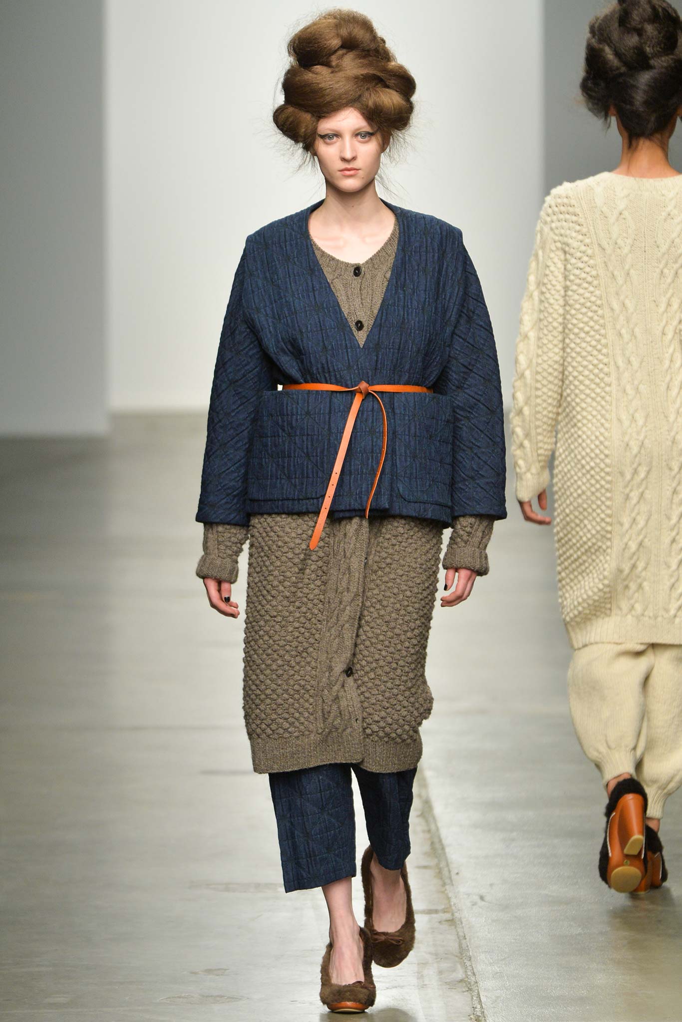 A relaxed blue cotton jacket with long sleeves and a layered design, paired with brown pants.